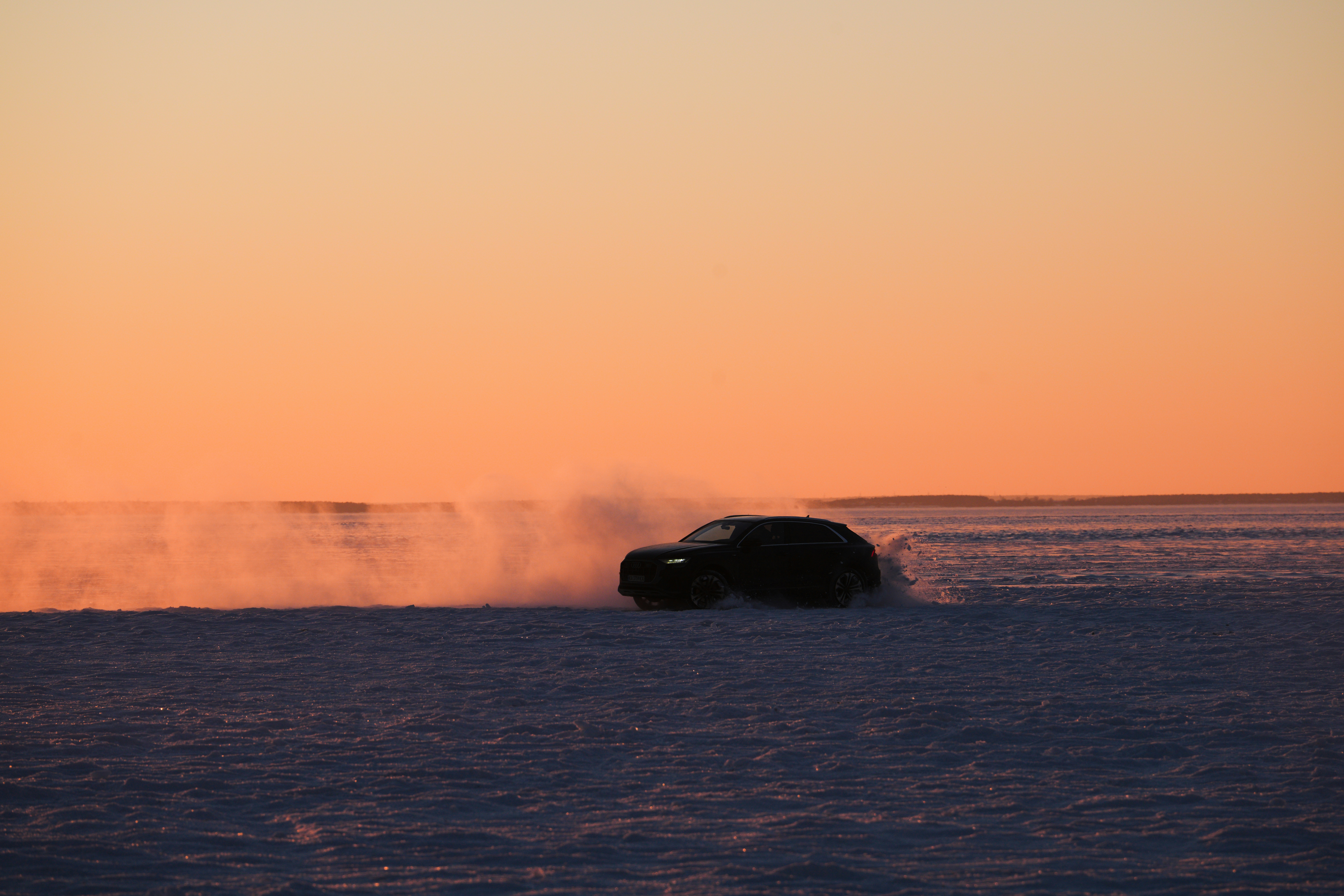 A car driving on a snowy plain at sunset