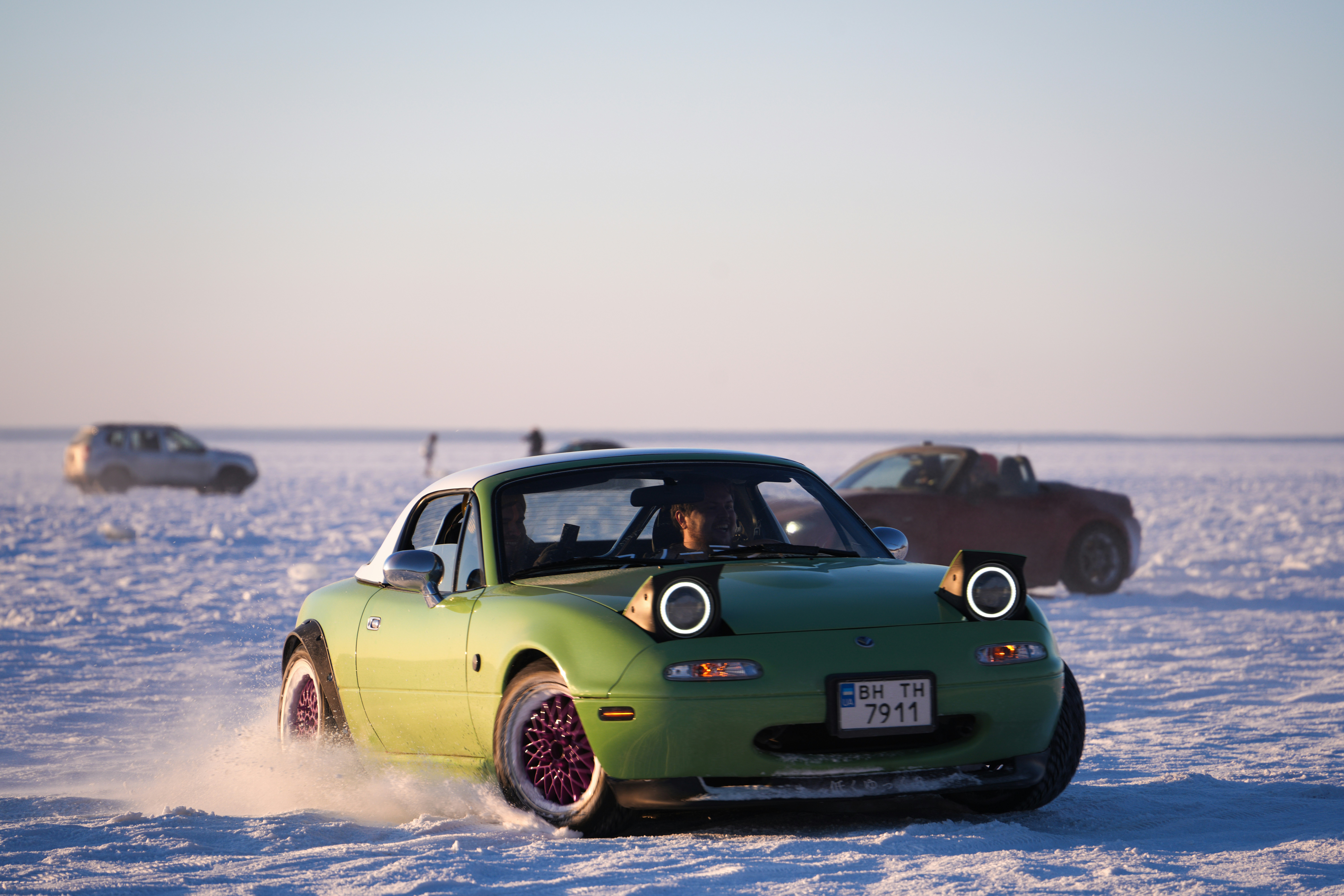 A green convertible car drifts on a snowy surface