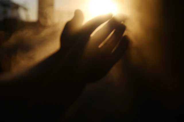 Hand reaching towards bright sunlight with dust particles