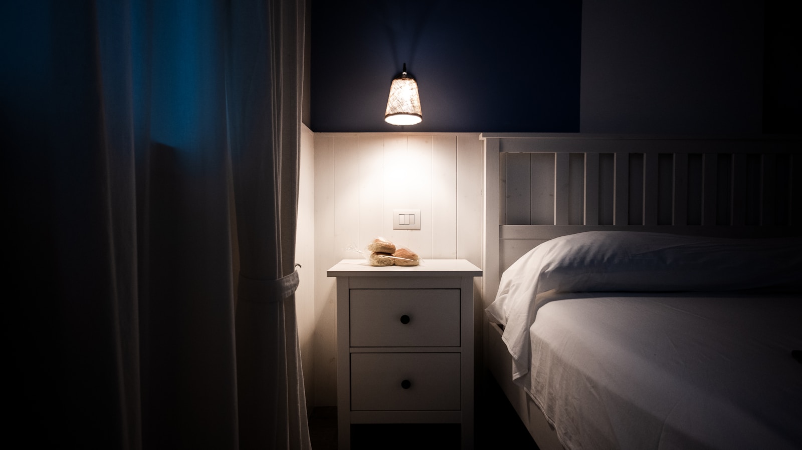 navy bedroom with white nightstand and small pendant lamp glow