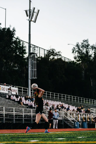 A female volleyball player serves the ball on a field.