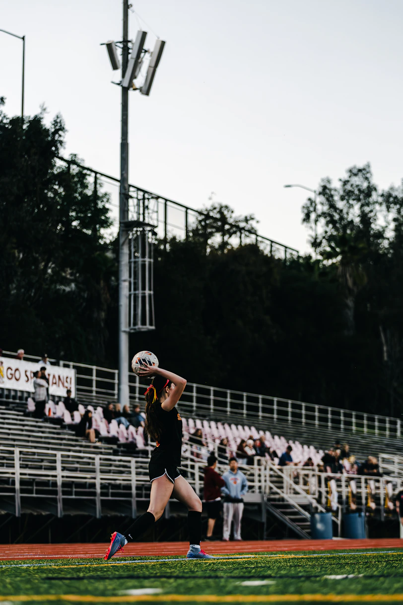 A female volleyball player serves the ball on a field.
