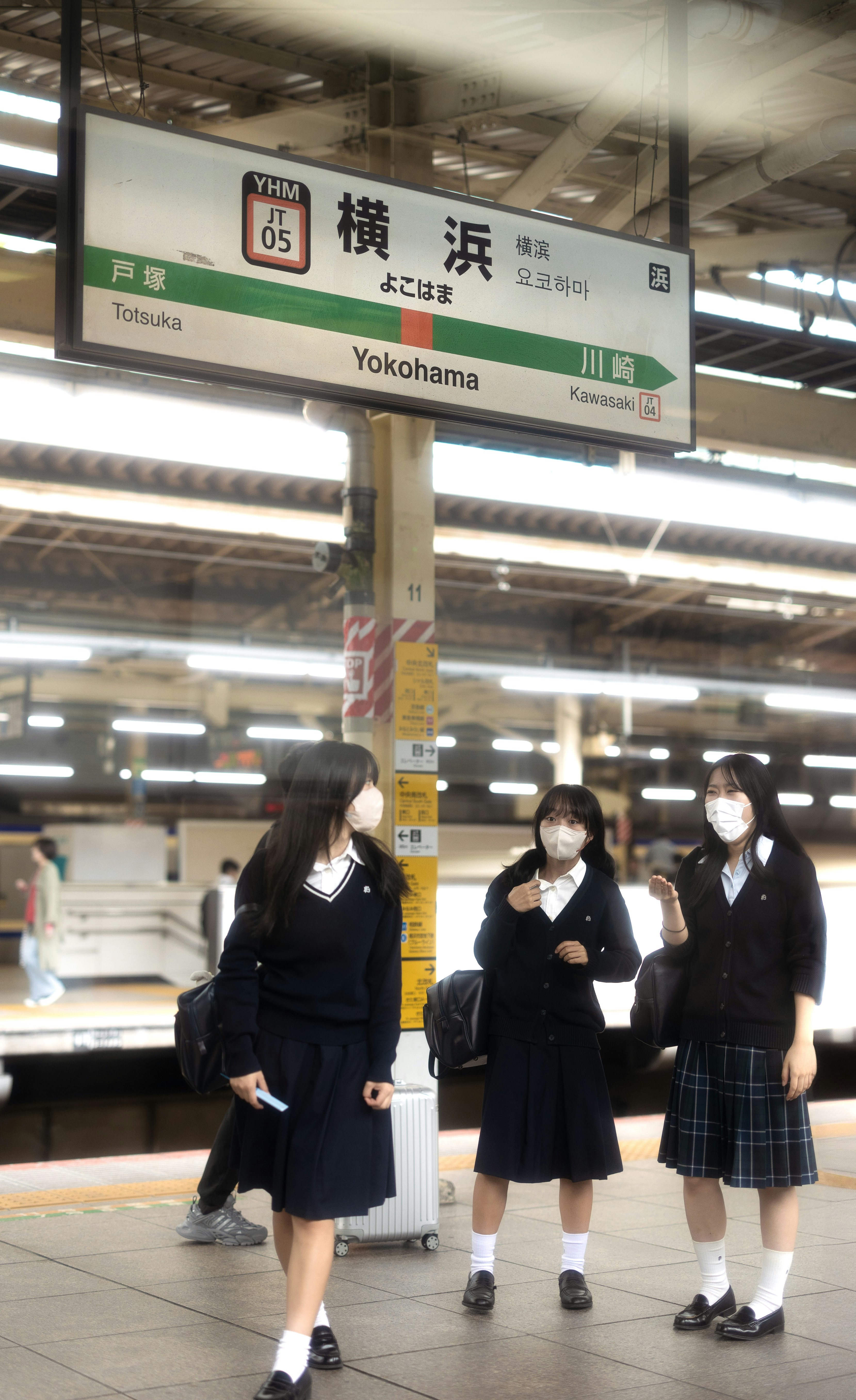 Three students in uniform wait at a train station.