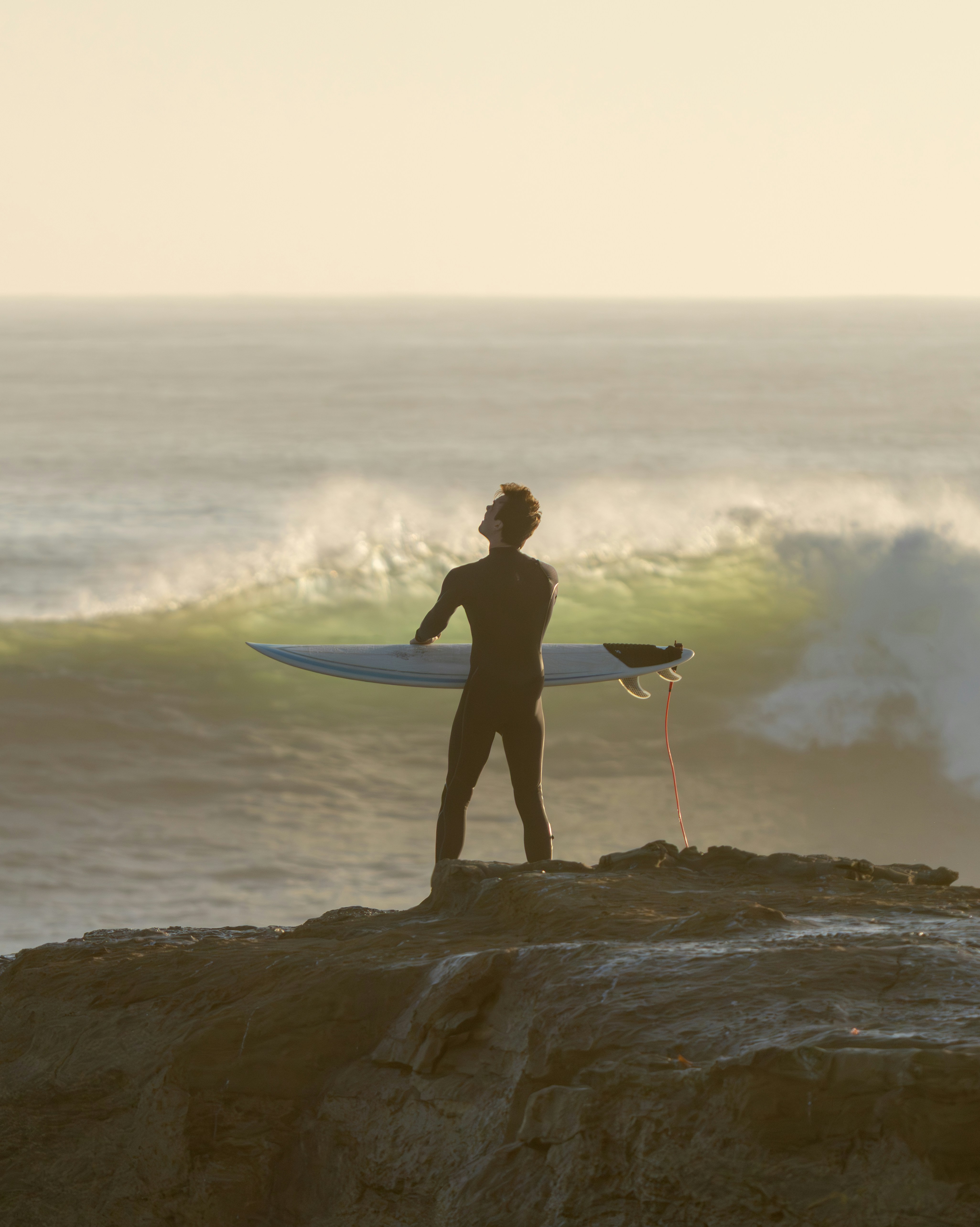 Surfer holding surfboard on cliff overlooking ocean waves
