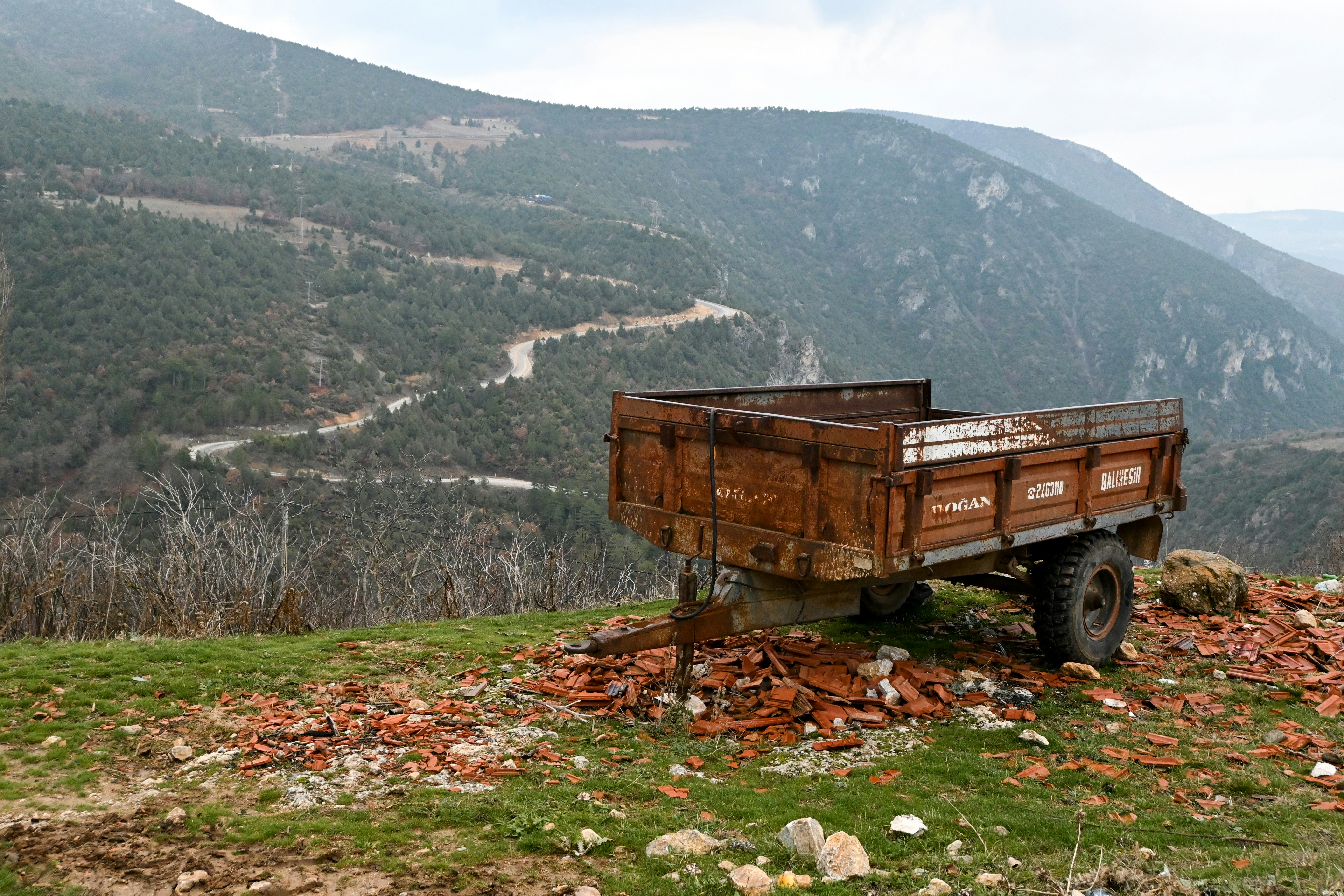 Old wooden trailer sits on a grassy hill.