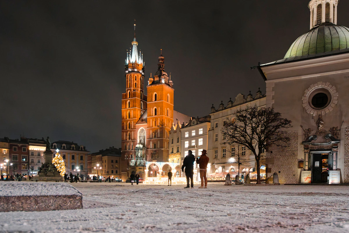 People crossing a snowy European square at night with a floodlit church behind them