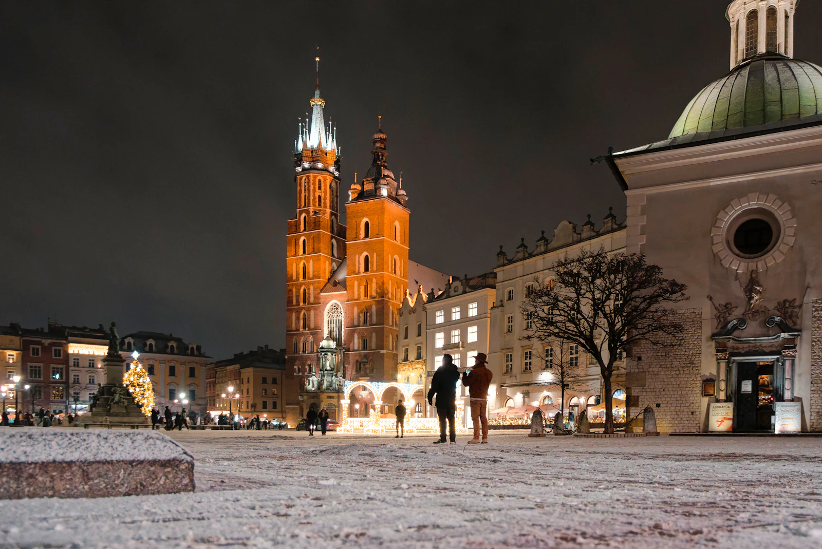 The twin towers of St. Mary's Basilica illuminated at night over Krakow's snow-covered Main Market Square in winter
