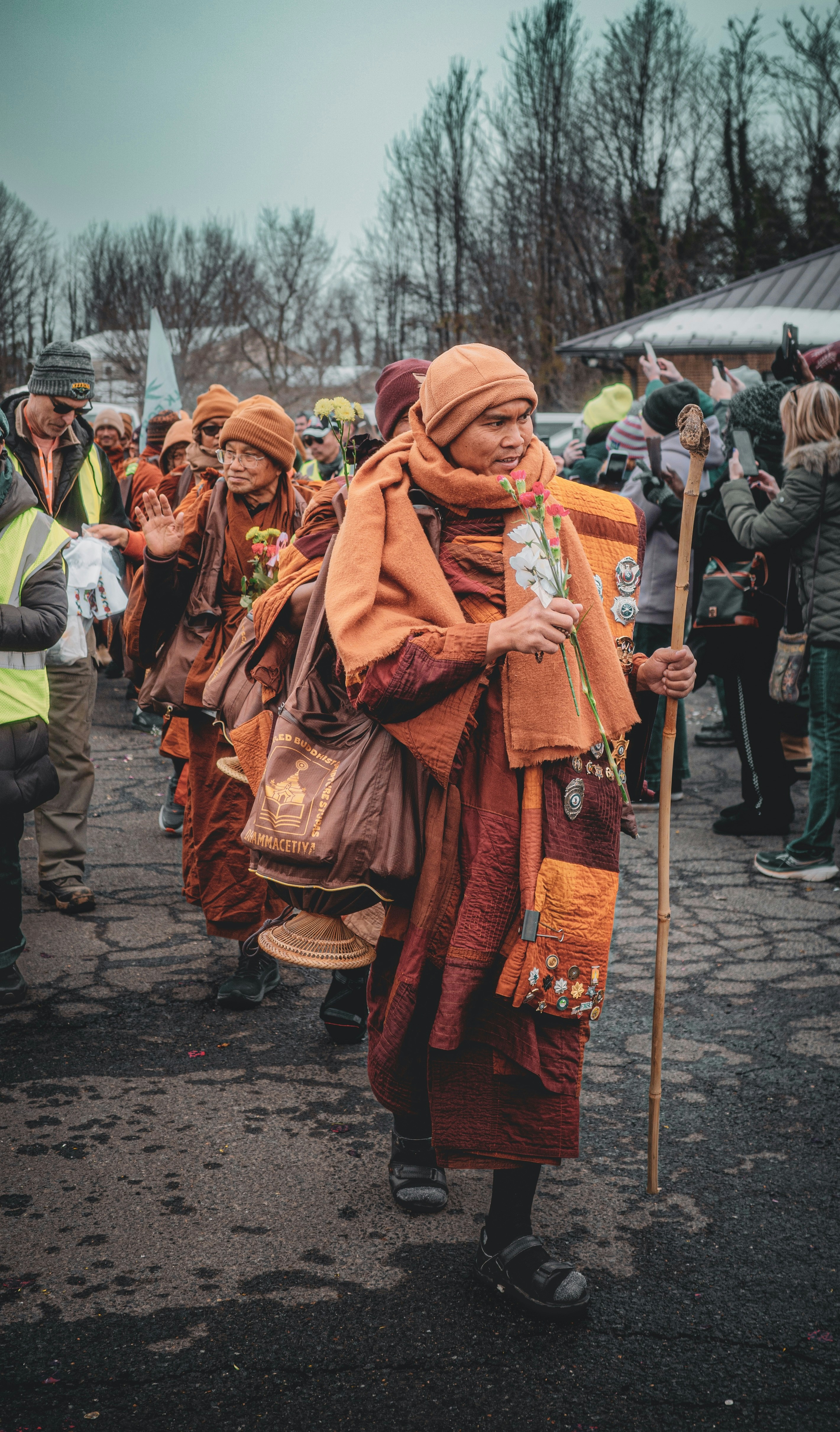 Monks in orange robes walk in procession with staffs.