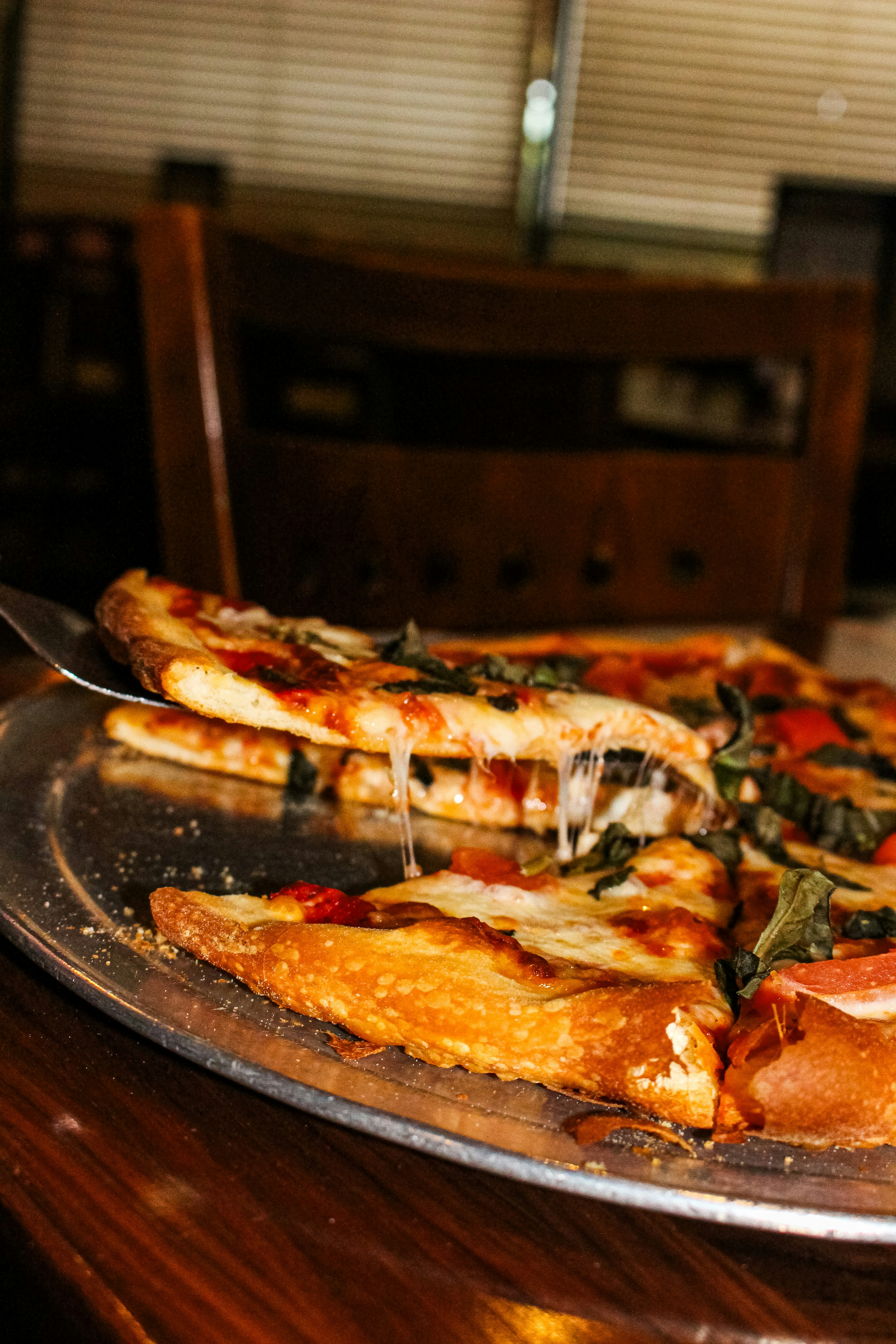 A slice of pizza being lifted from a metal tray.