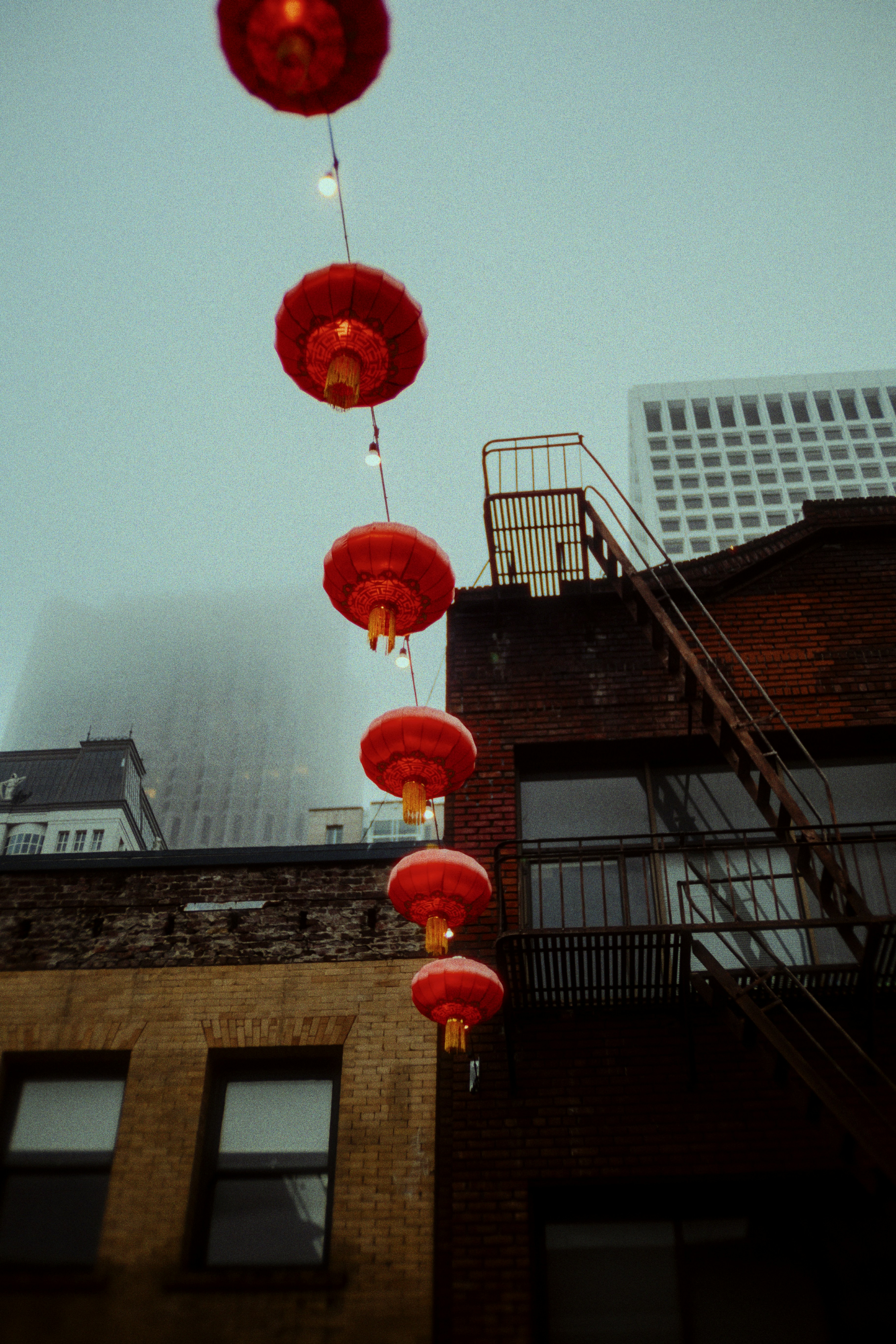 Red lanterns strung between buildings on a foggy day