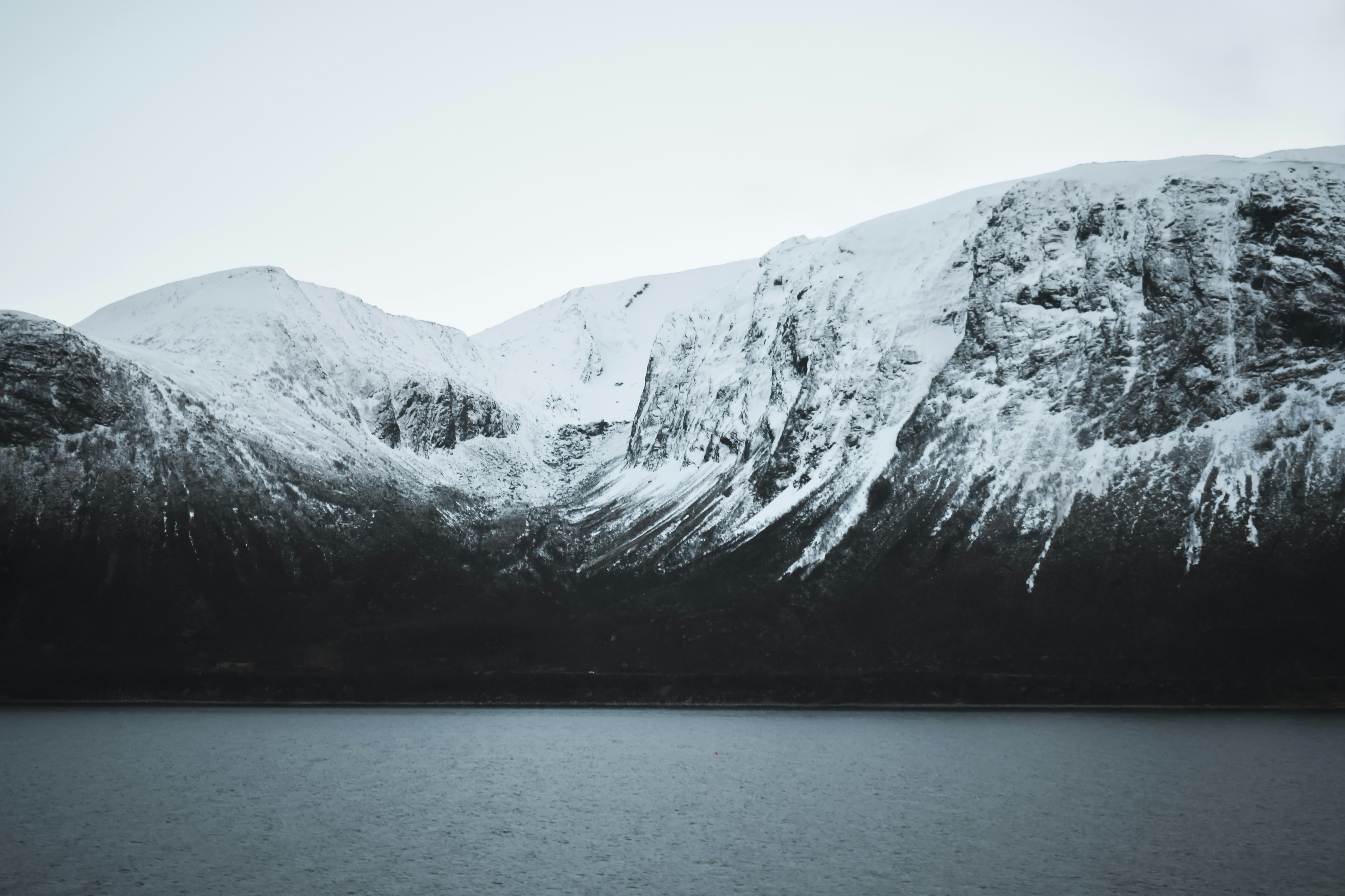 Snow-covered mountains rise above a dark, calm body of water.