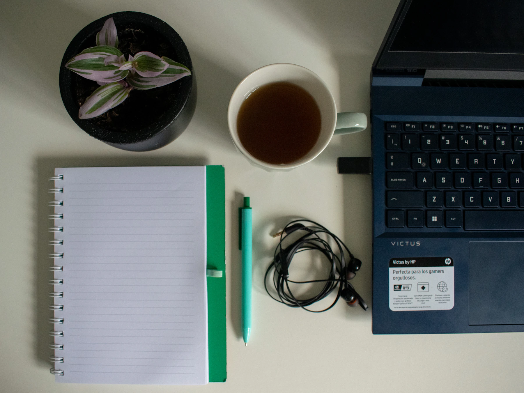 Laptop, notebook, pen, earphones and tea arranged across a clean technology workspace
