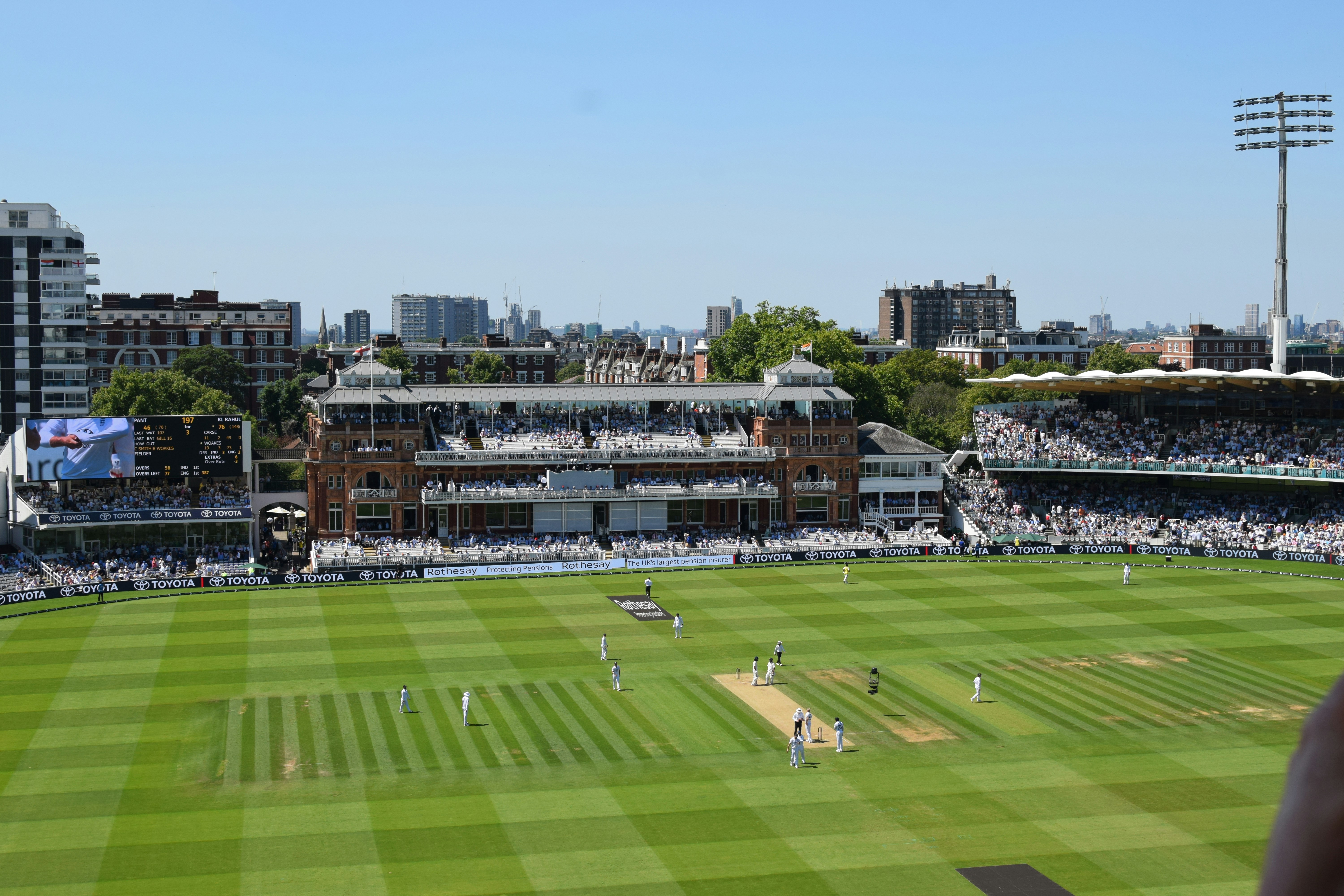 A cricket match is underway at a sunny stadium.