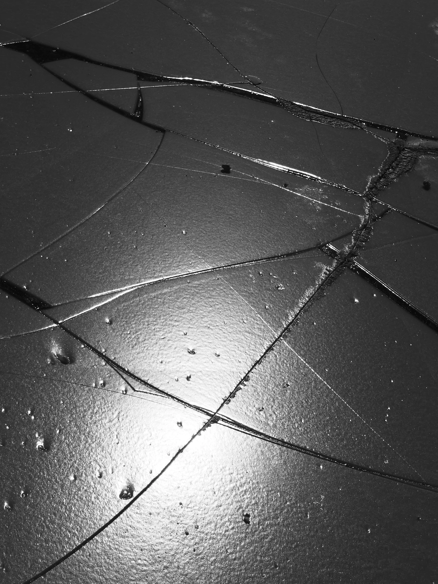 A black glass panel split by a radiating crack, lit from one side