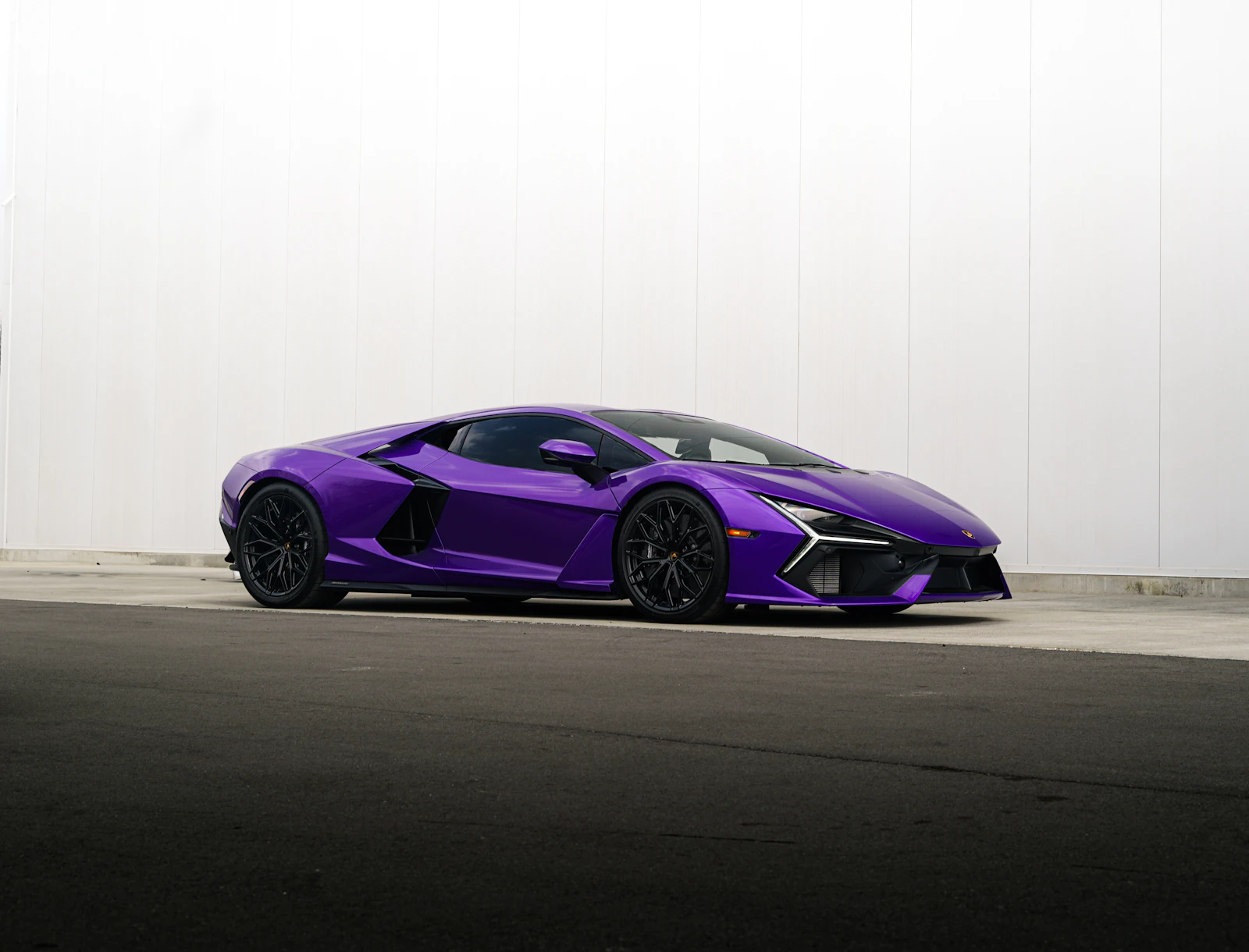Purple Lamborghini Revuelto parked against a white wall