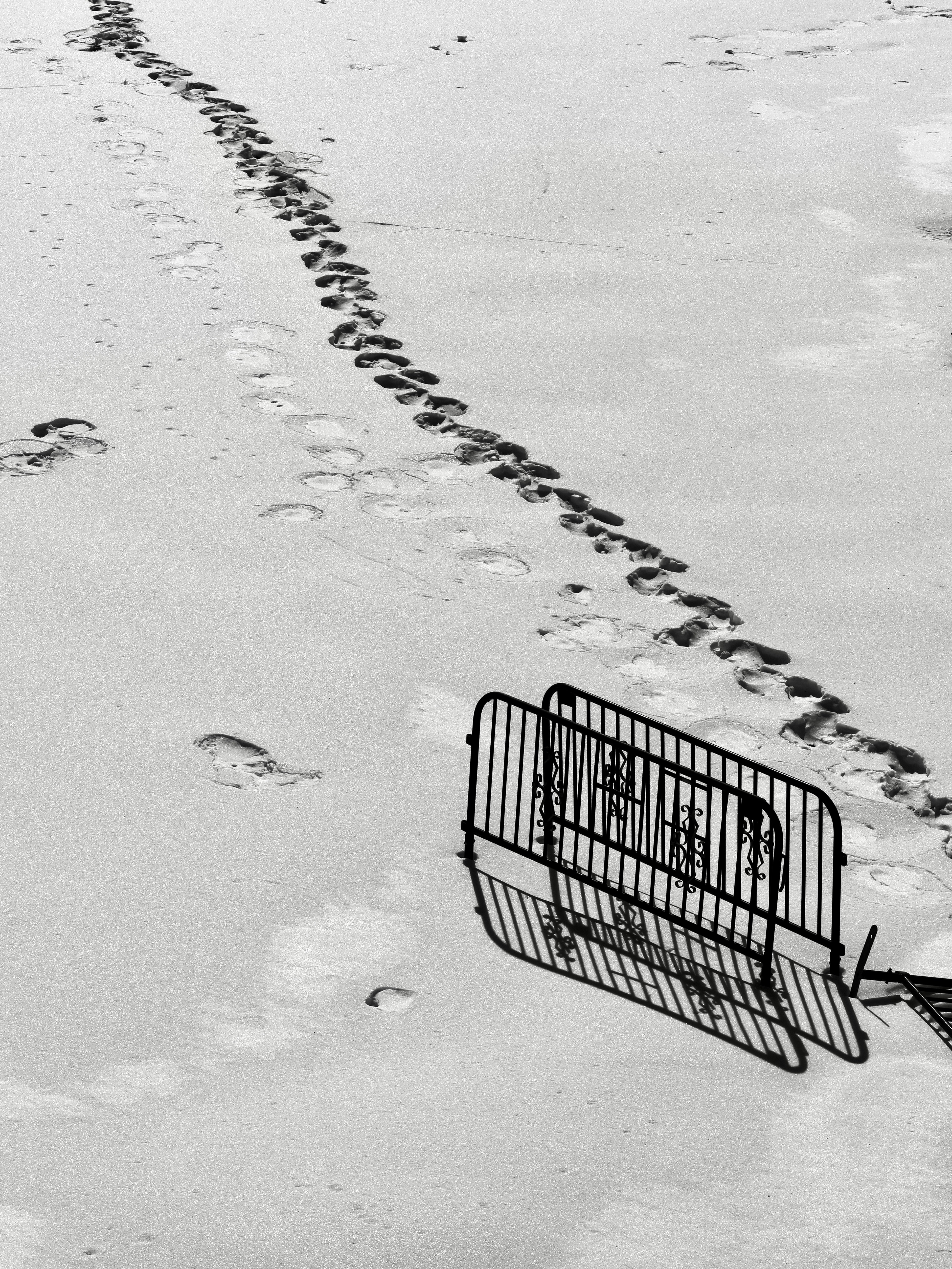 Footprints lead past a metal barrier on a sandy surface