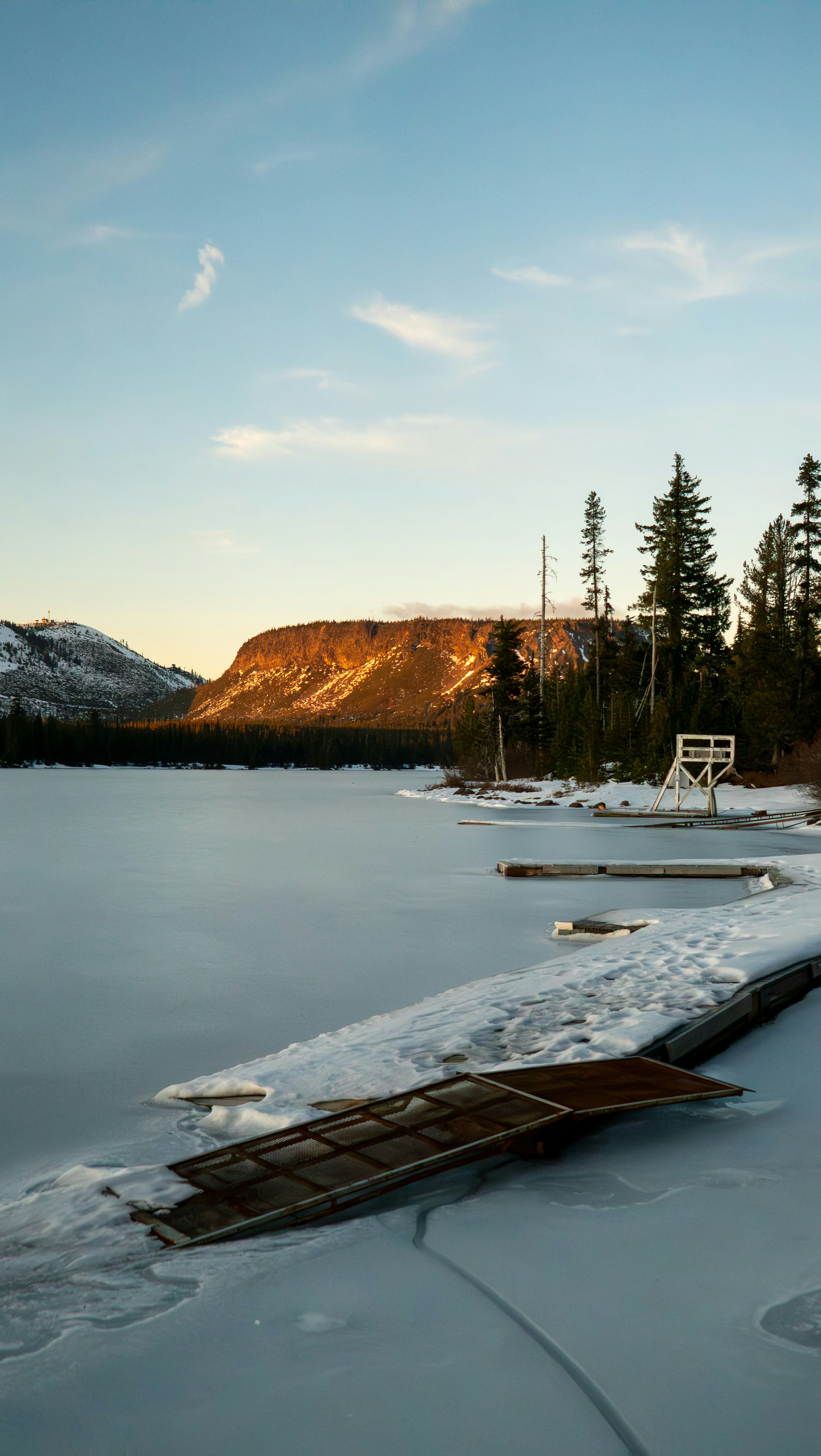 凍った湖と桟橋、日差しの差し込む山の背景。