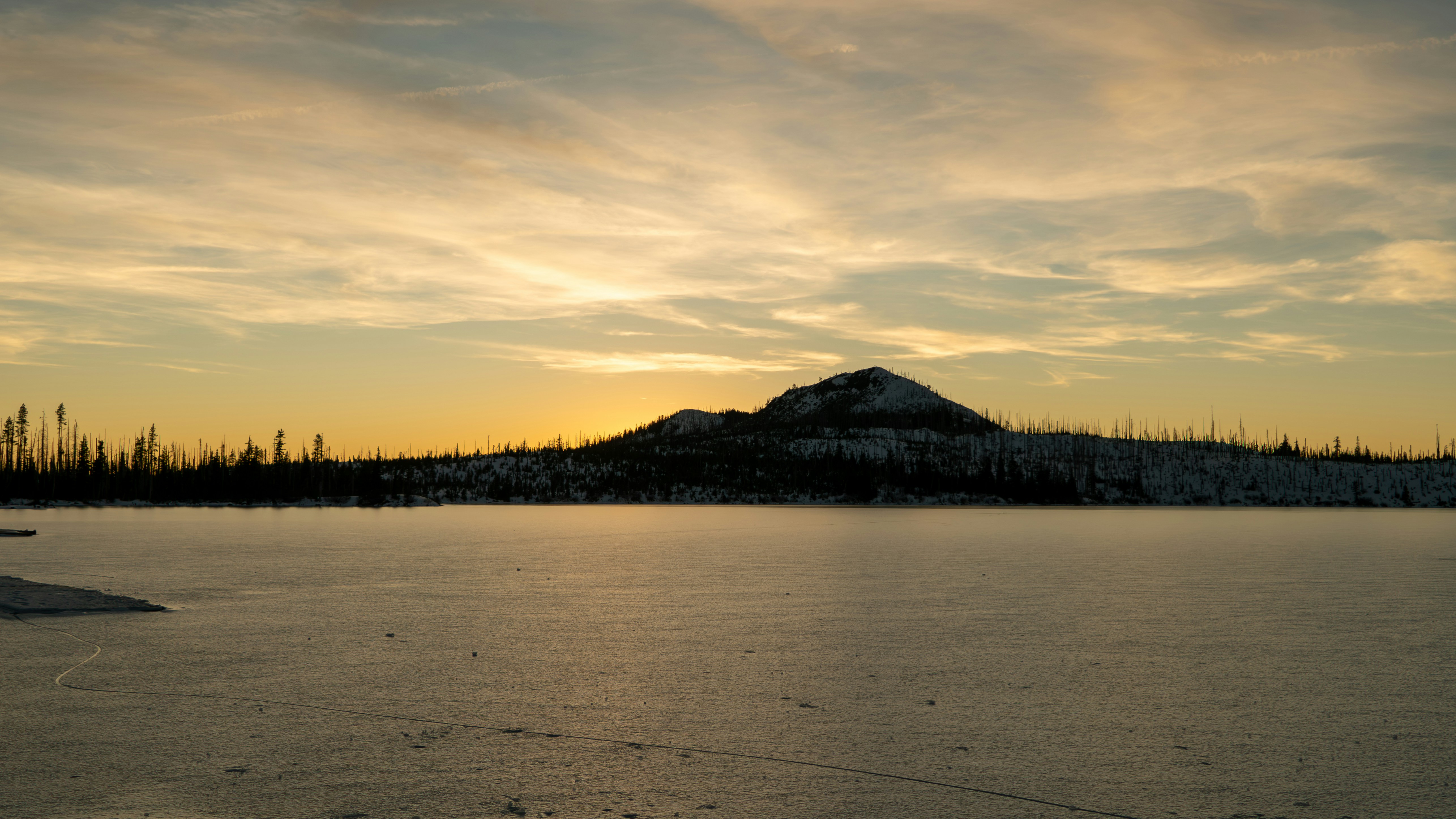 凍った湖の上に山のシルエットが映る夕焼け