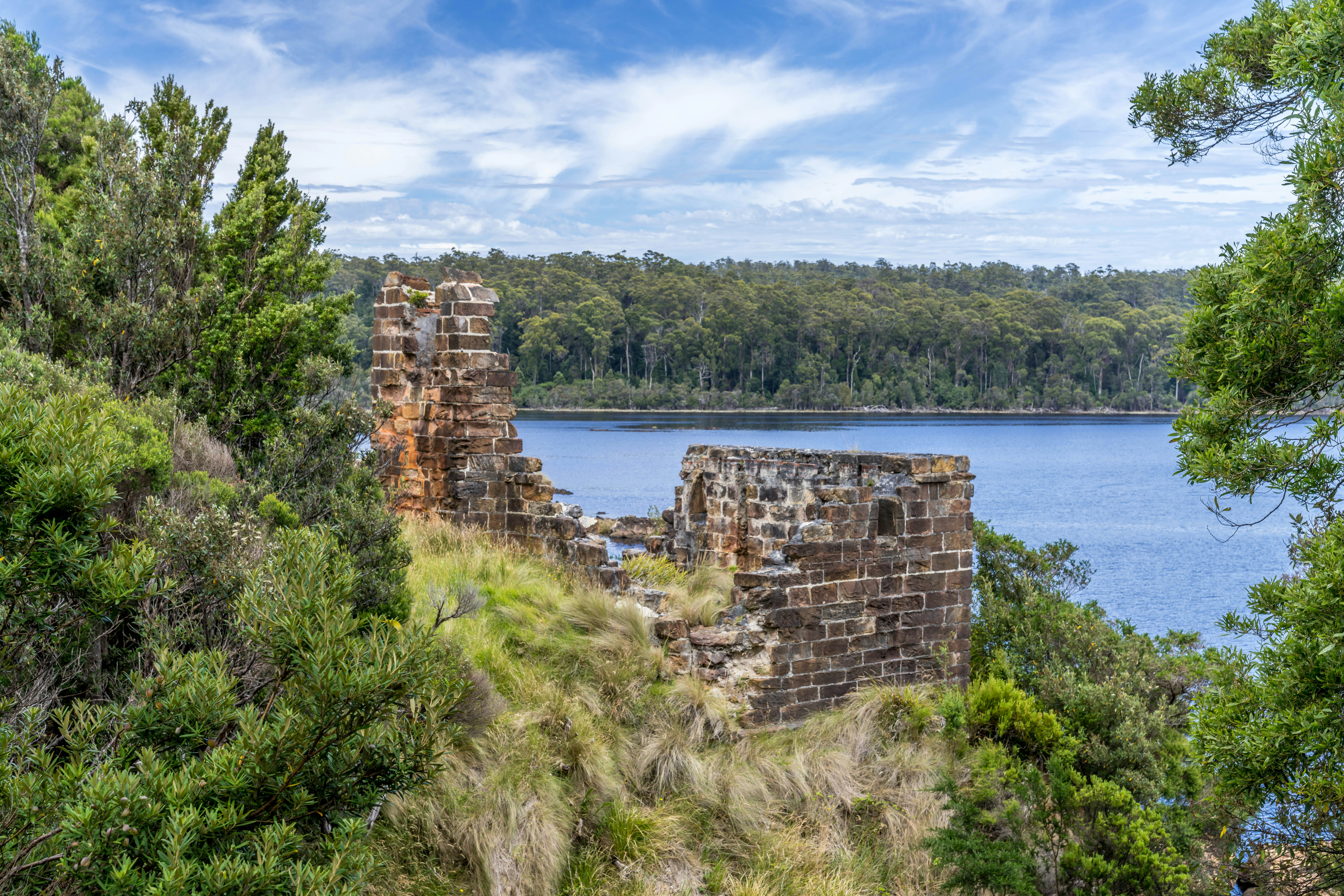 Ruinas de piedra en una colina cubierta de hierba con vistas a un lago azul.