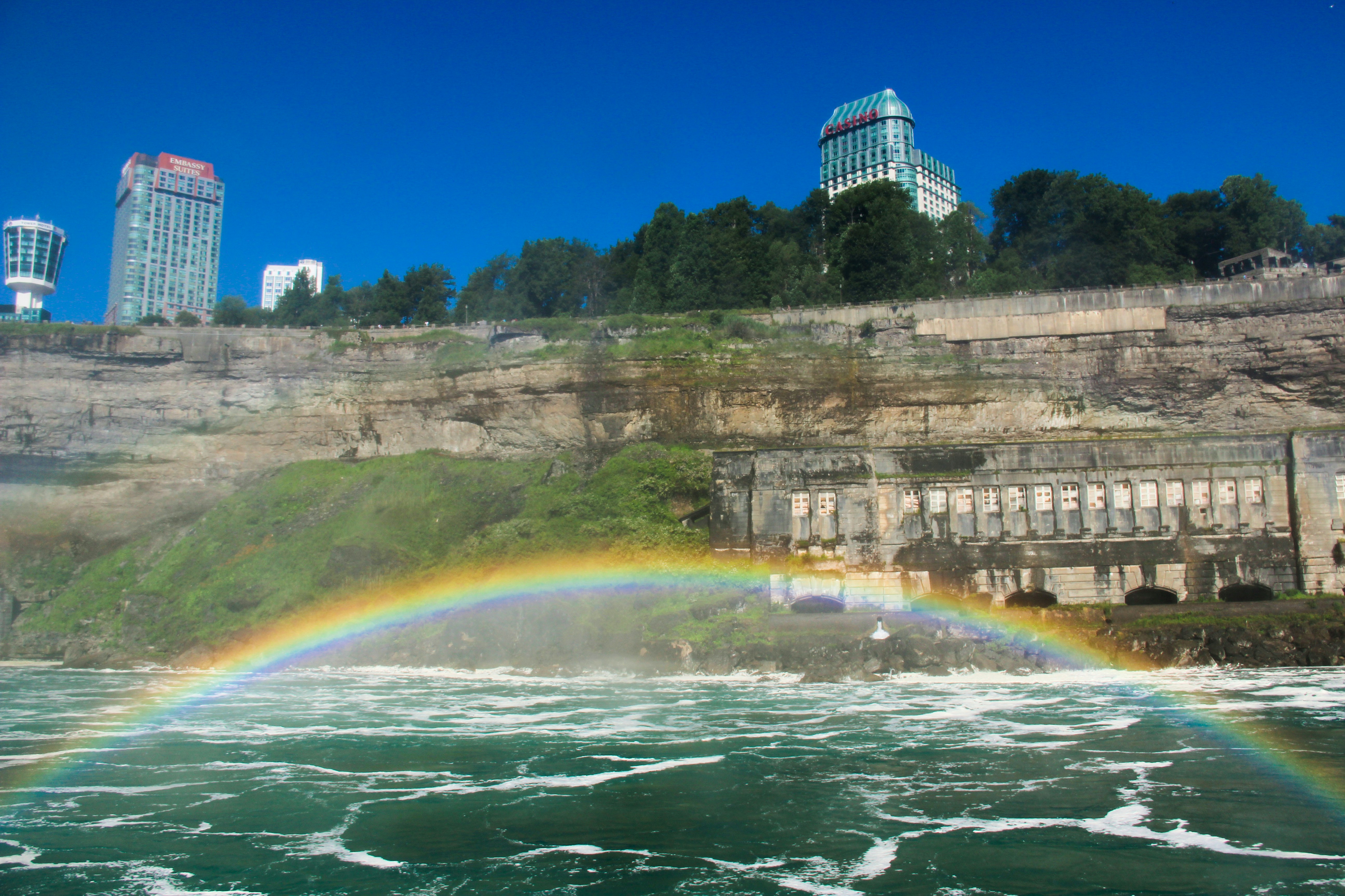 Rainbow over niagara falls with buildings on cliff.