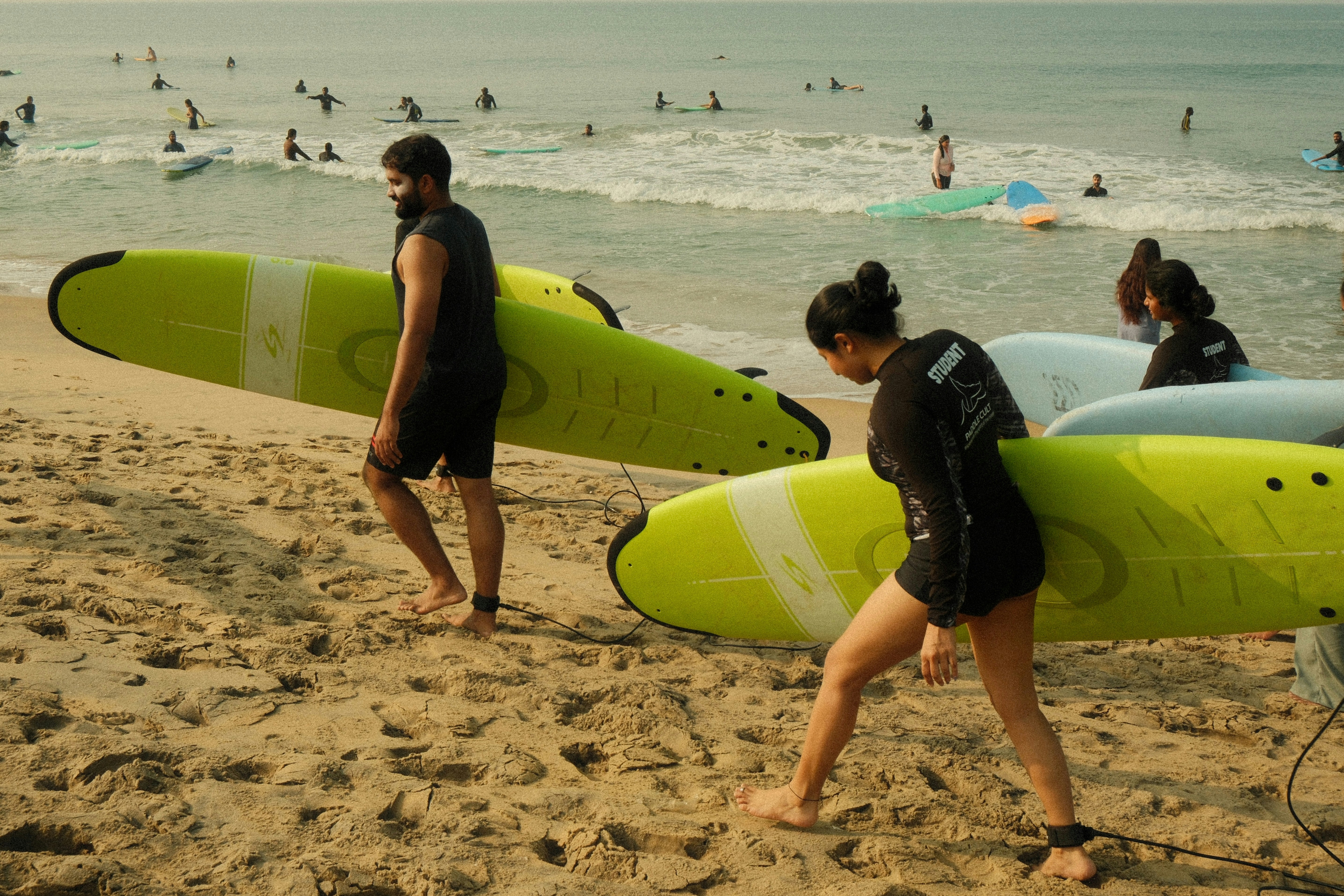 Surfers carrying surfboards on a sandy beach.