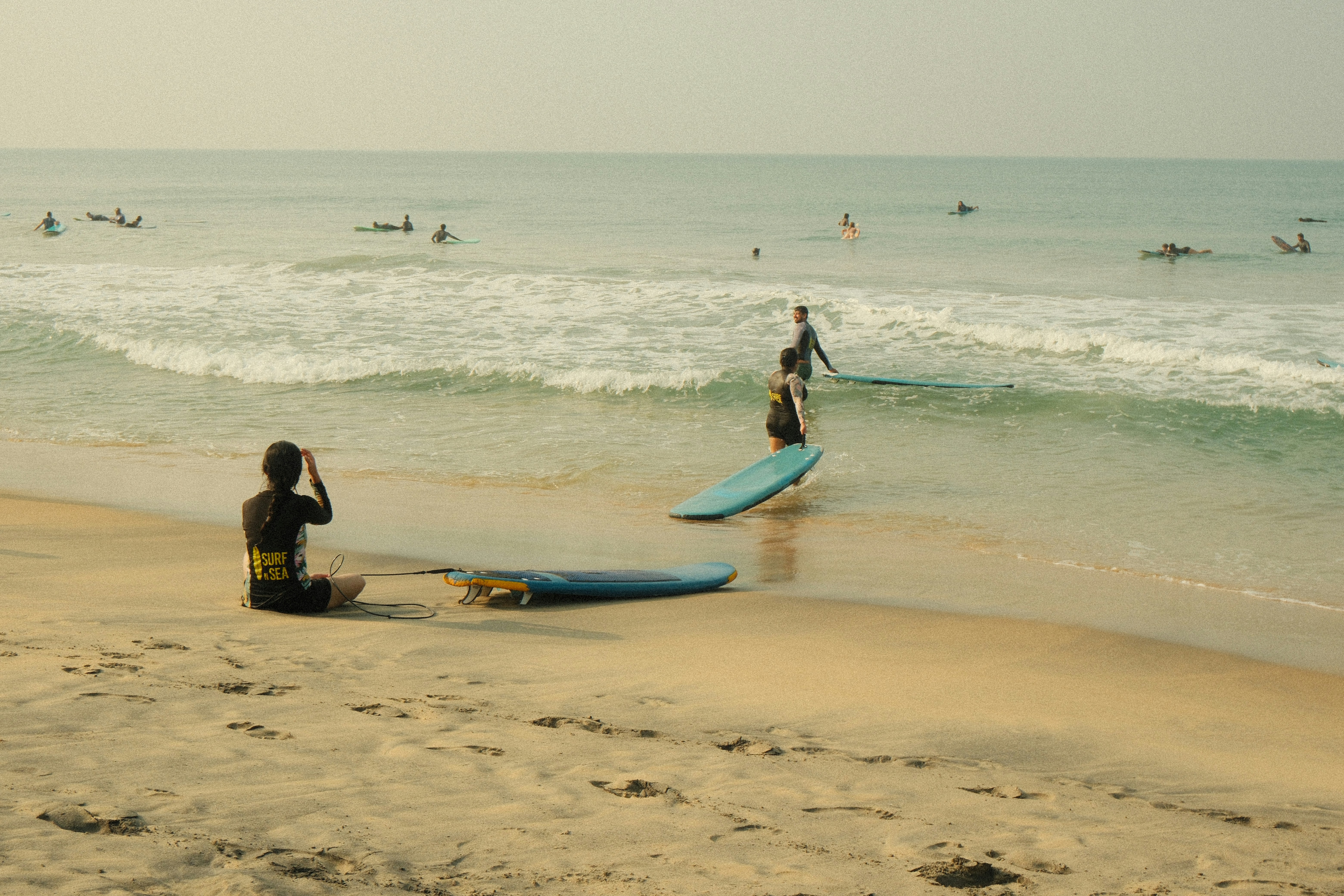 Surfers paddle in the ocean near a sandy beach.