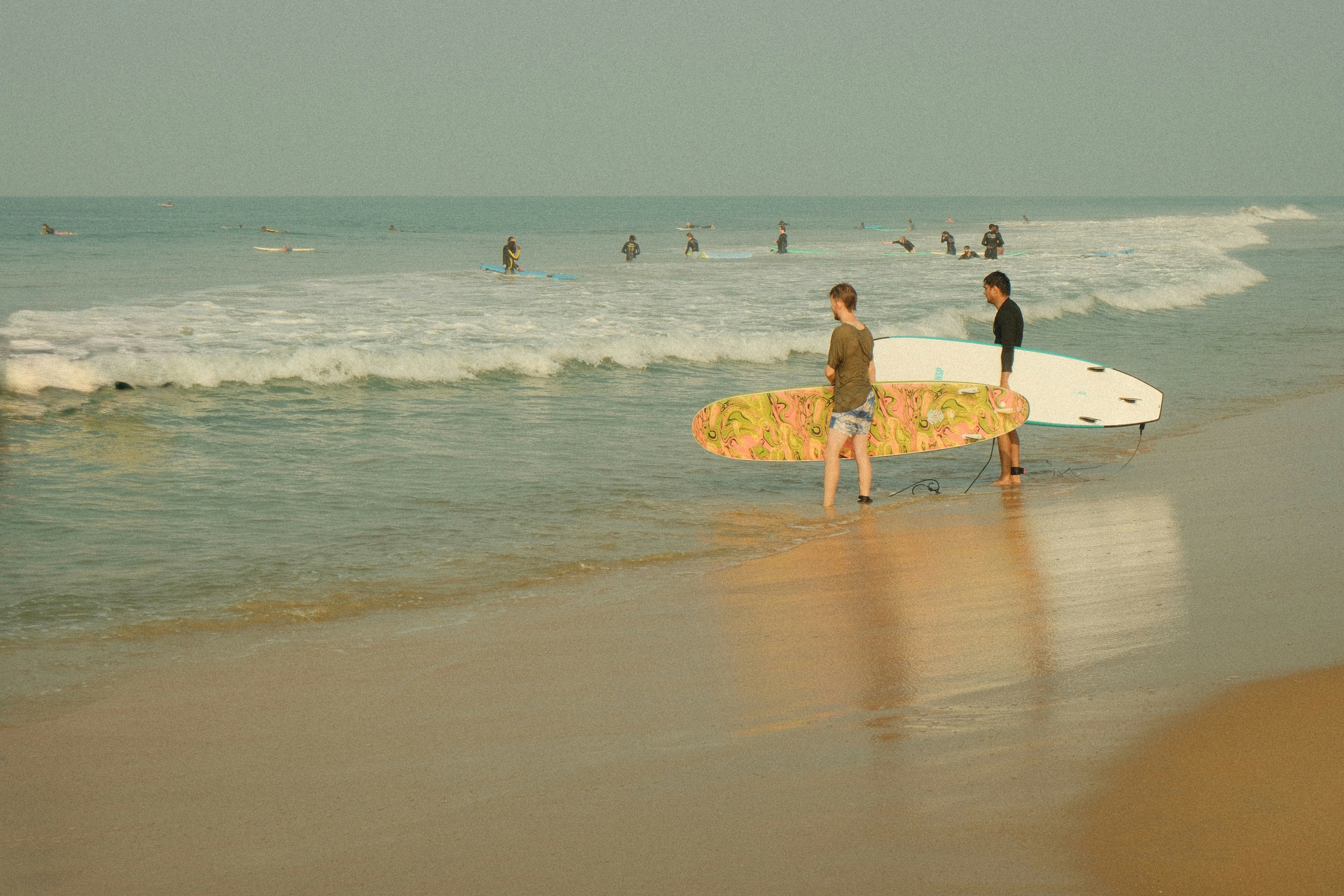 Two surfers carrying surfboards on a sandy beach.