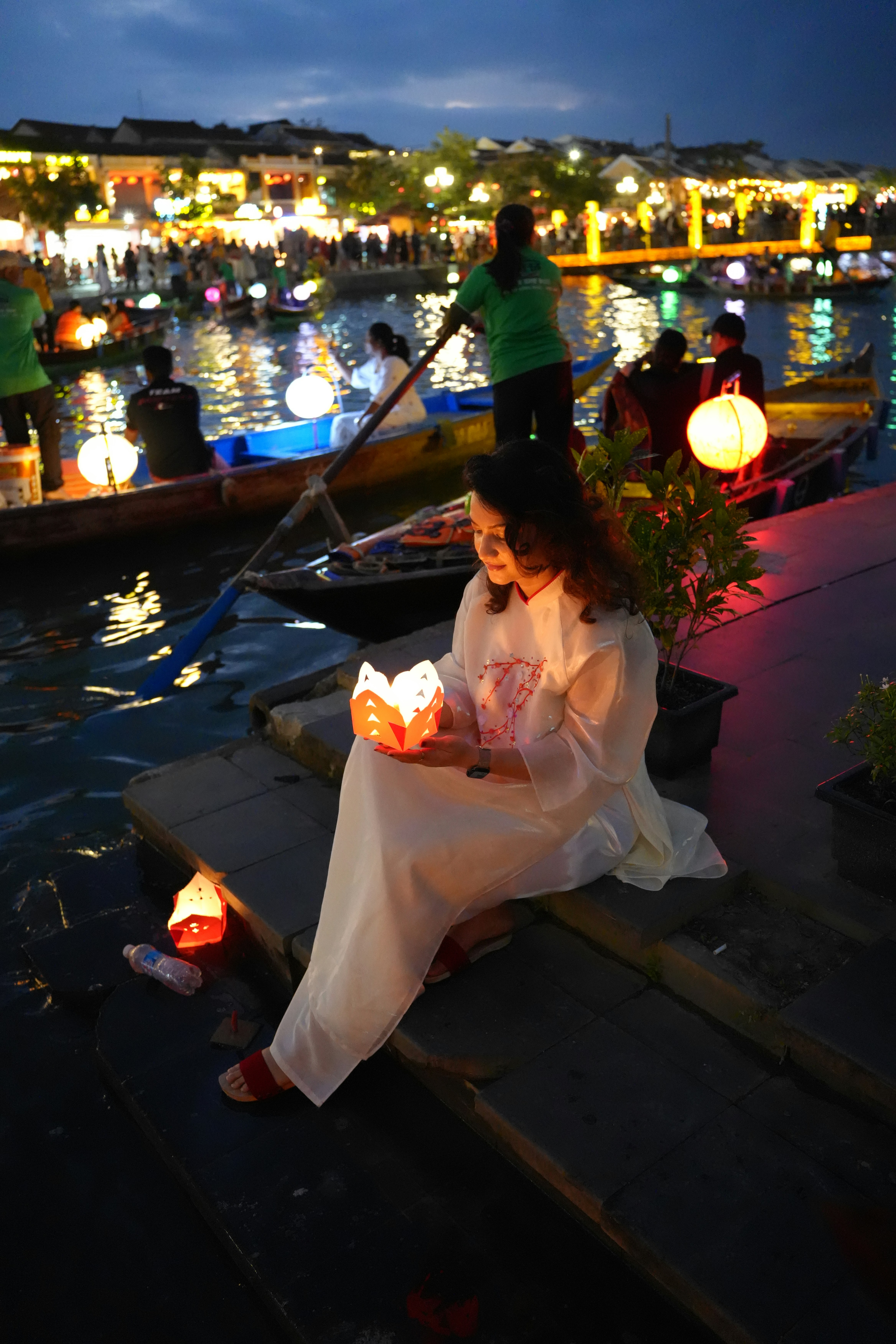 Woman holding a lotus lantern by a river at night.