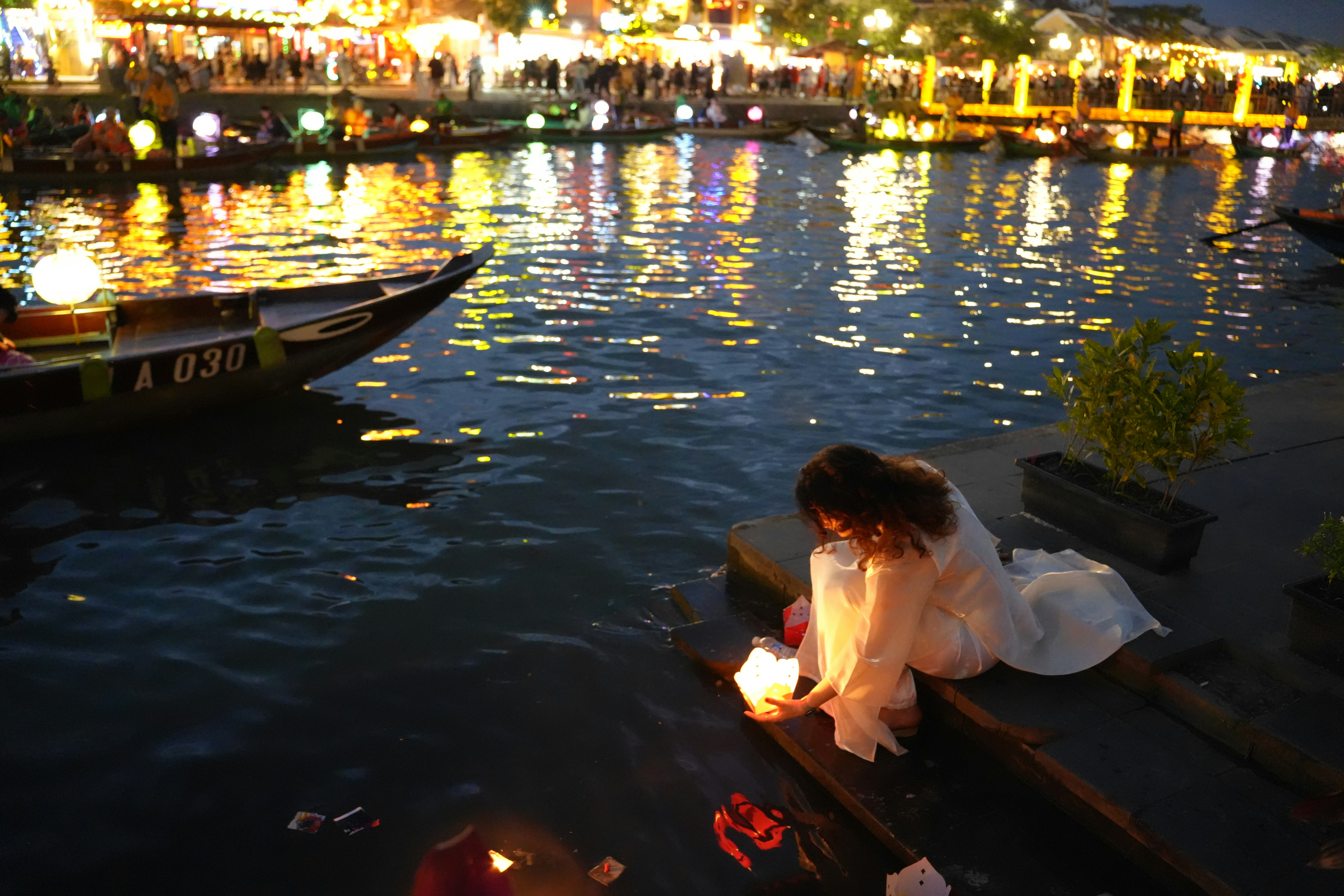 Woman lights lantern by a river at night
