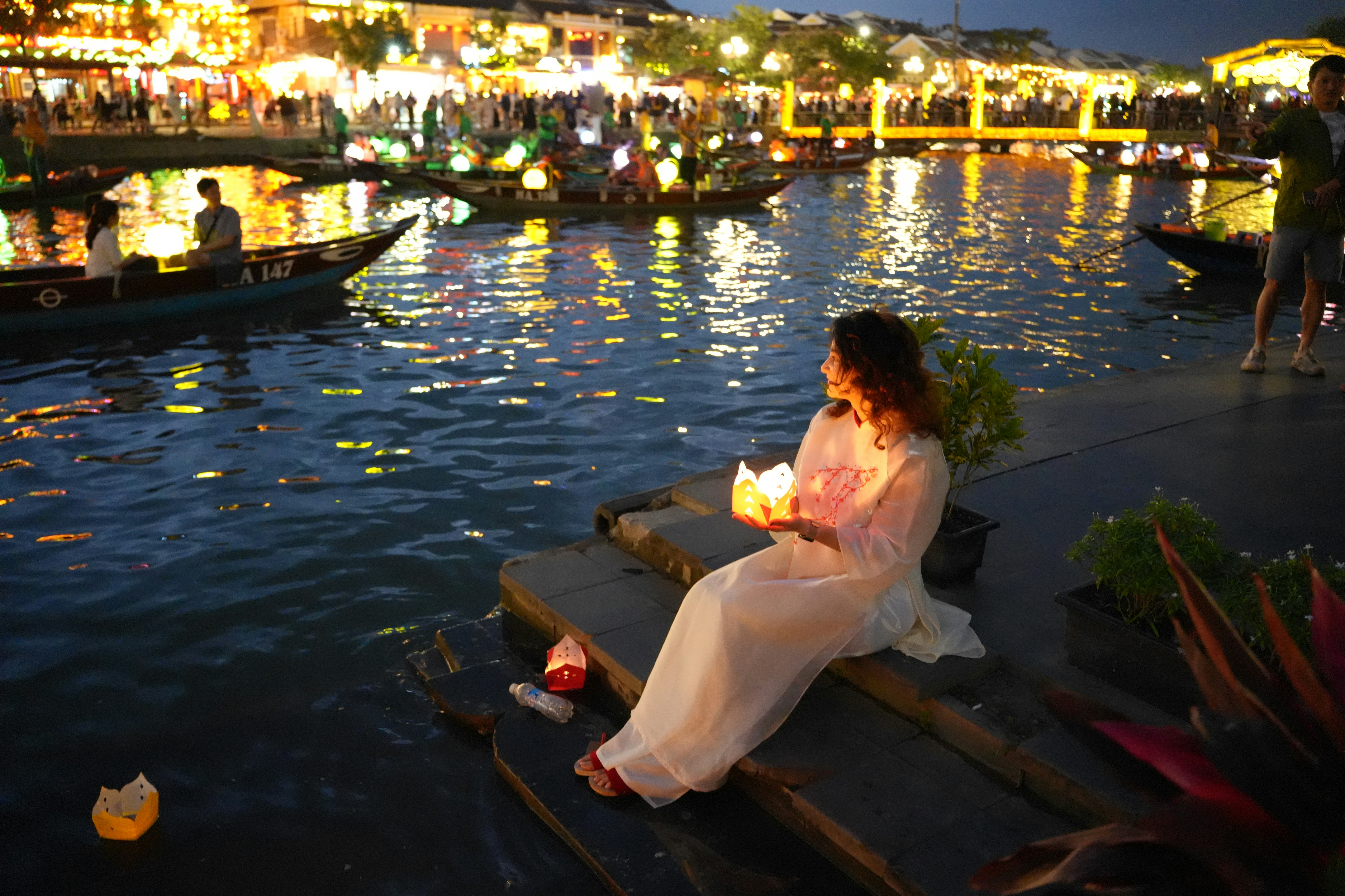 Woman holding lantern by river at night