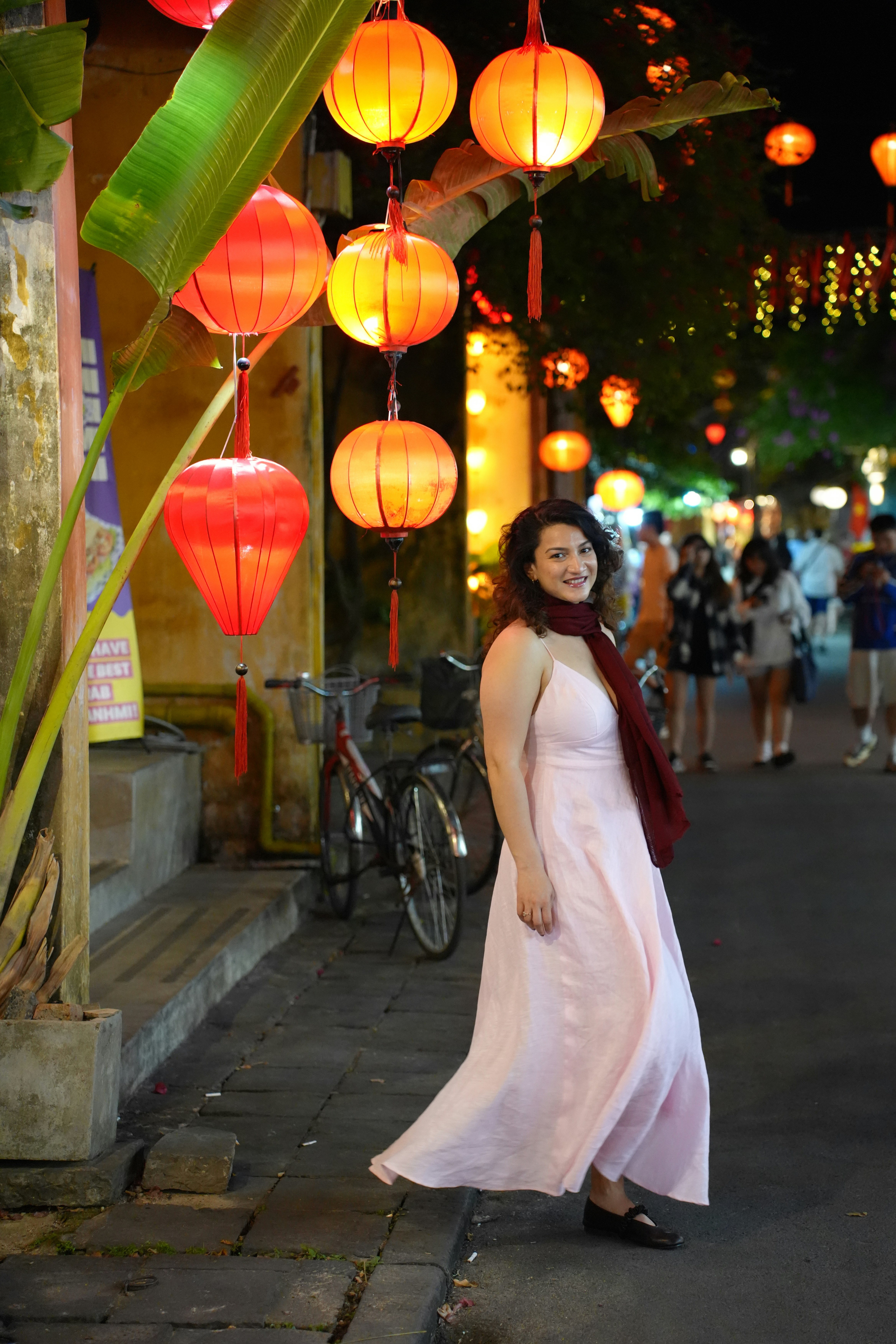 Woman in pink dress smiles under red lanterns at night