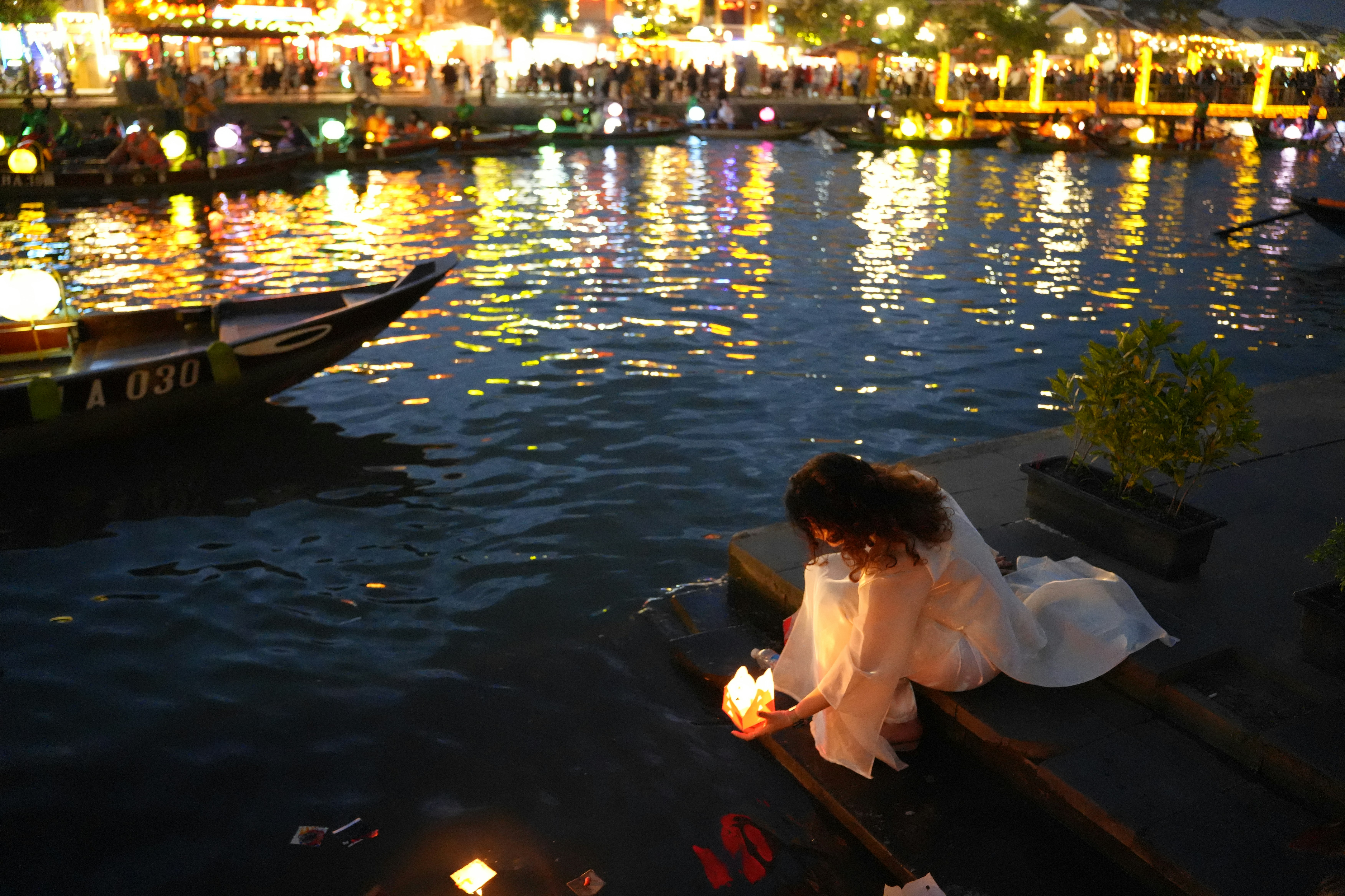 Woman holding lantern by water at night