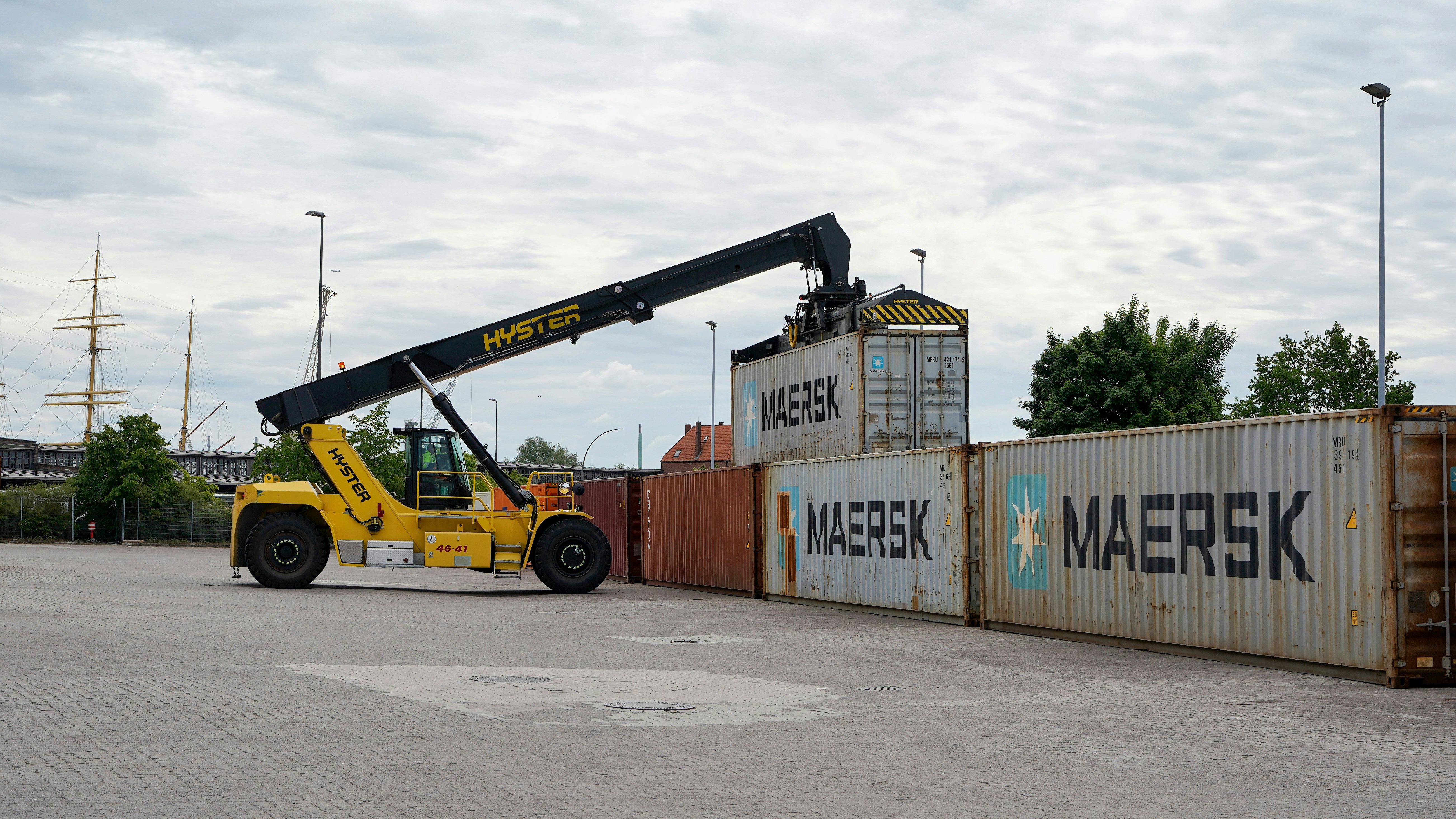 A yellow reach stacker lifts a shipping container.