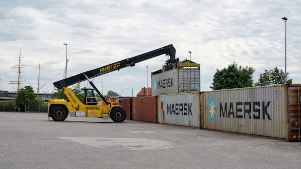 A yellow reach stacker lifts a shipping container.