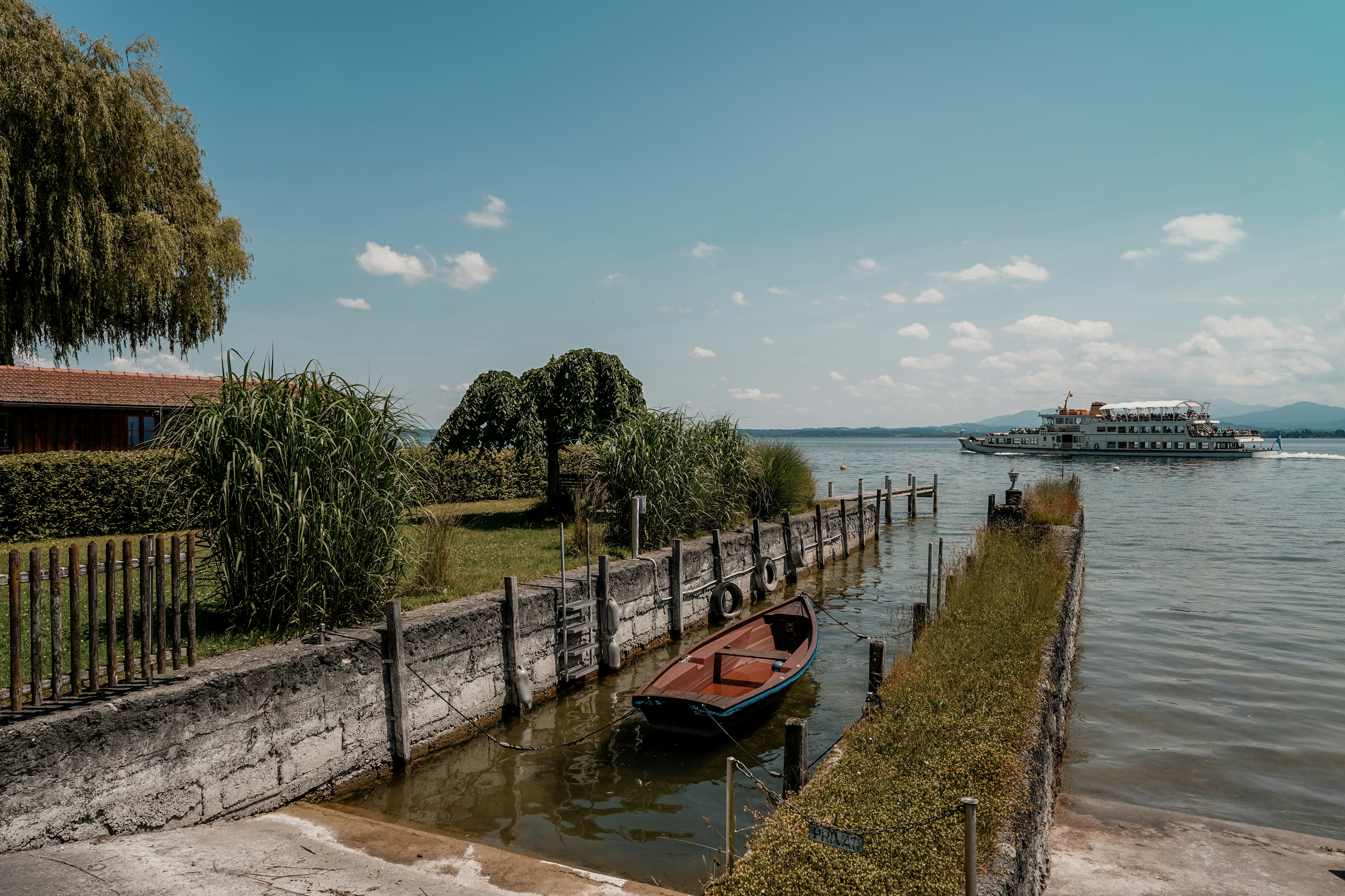 A small boat docked by a lake with a ferry