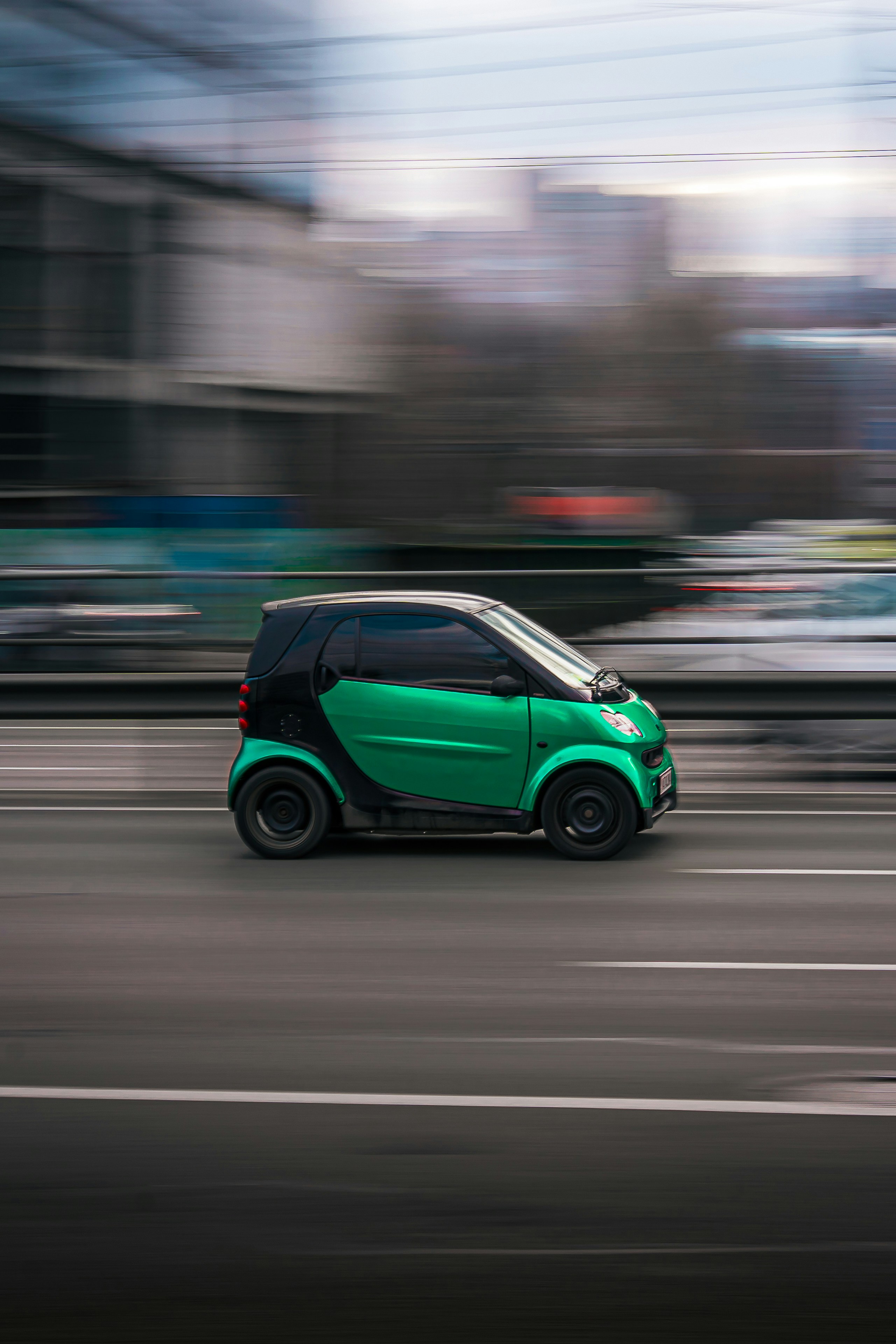 A small green car speeding down a blurred street