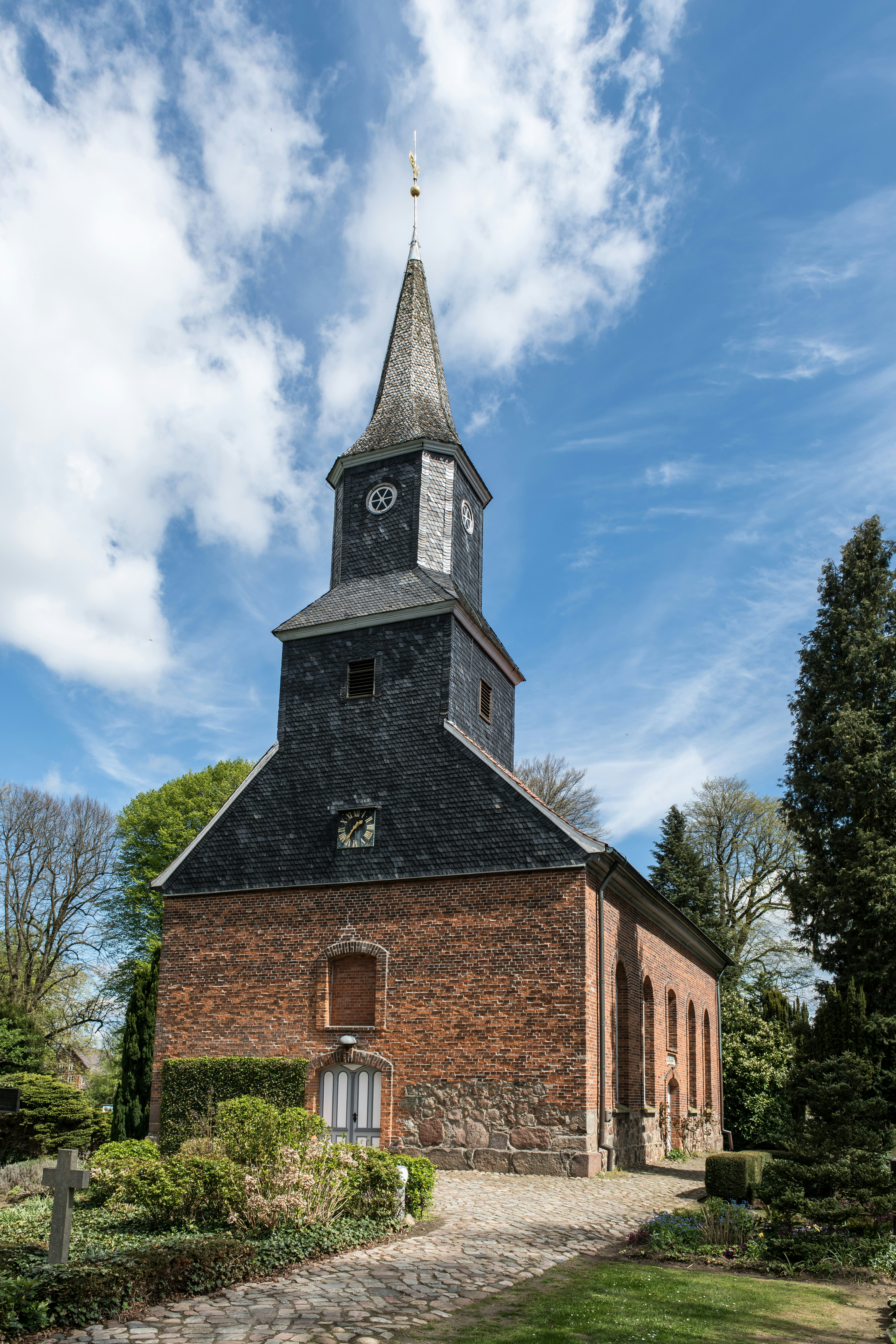 Brick church with a tall spire under a cloudy sky