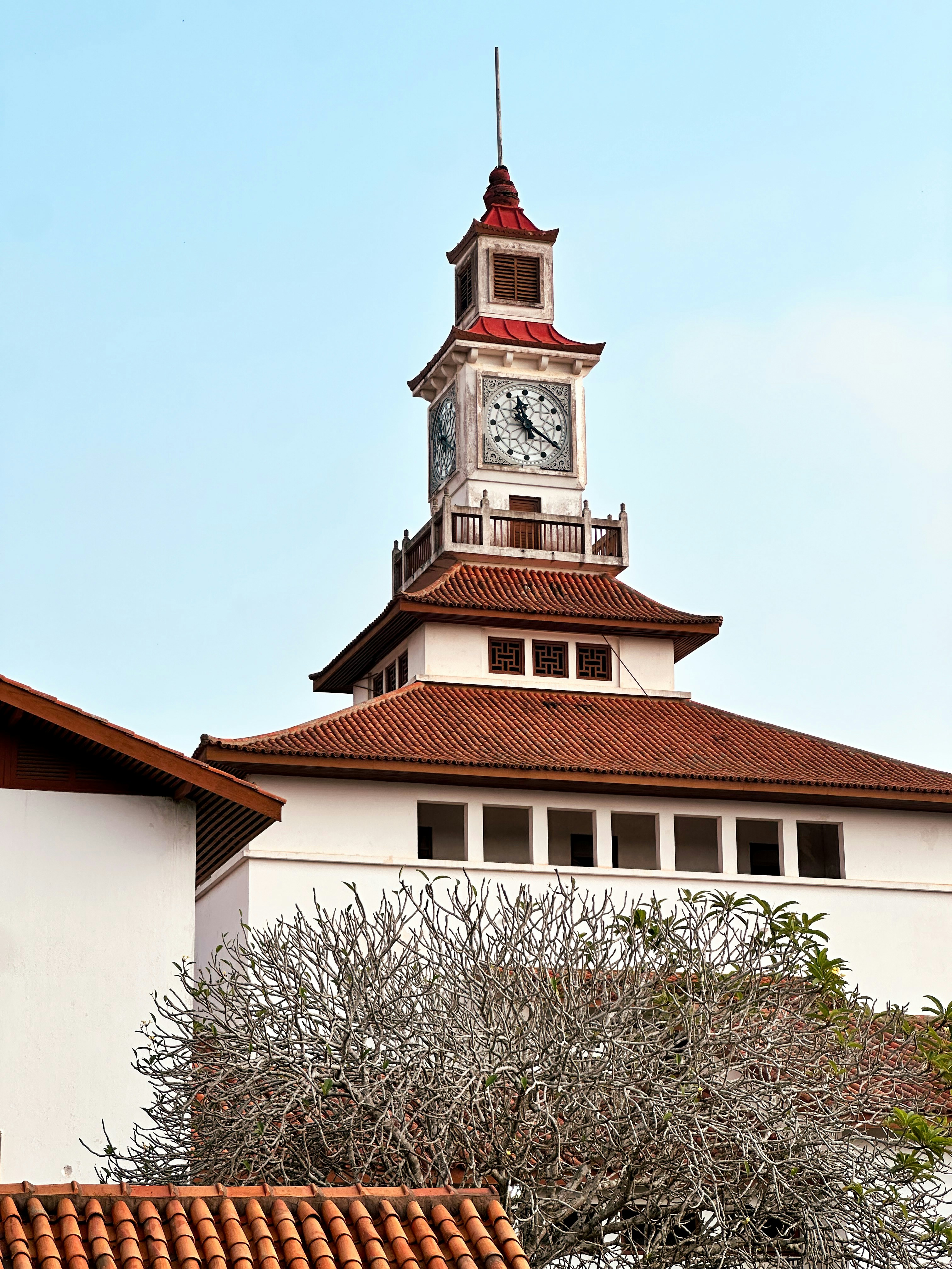 Un bâtiment blanc avec un toit en tuiles rouges et une tour d’horloge.