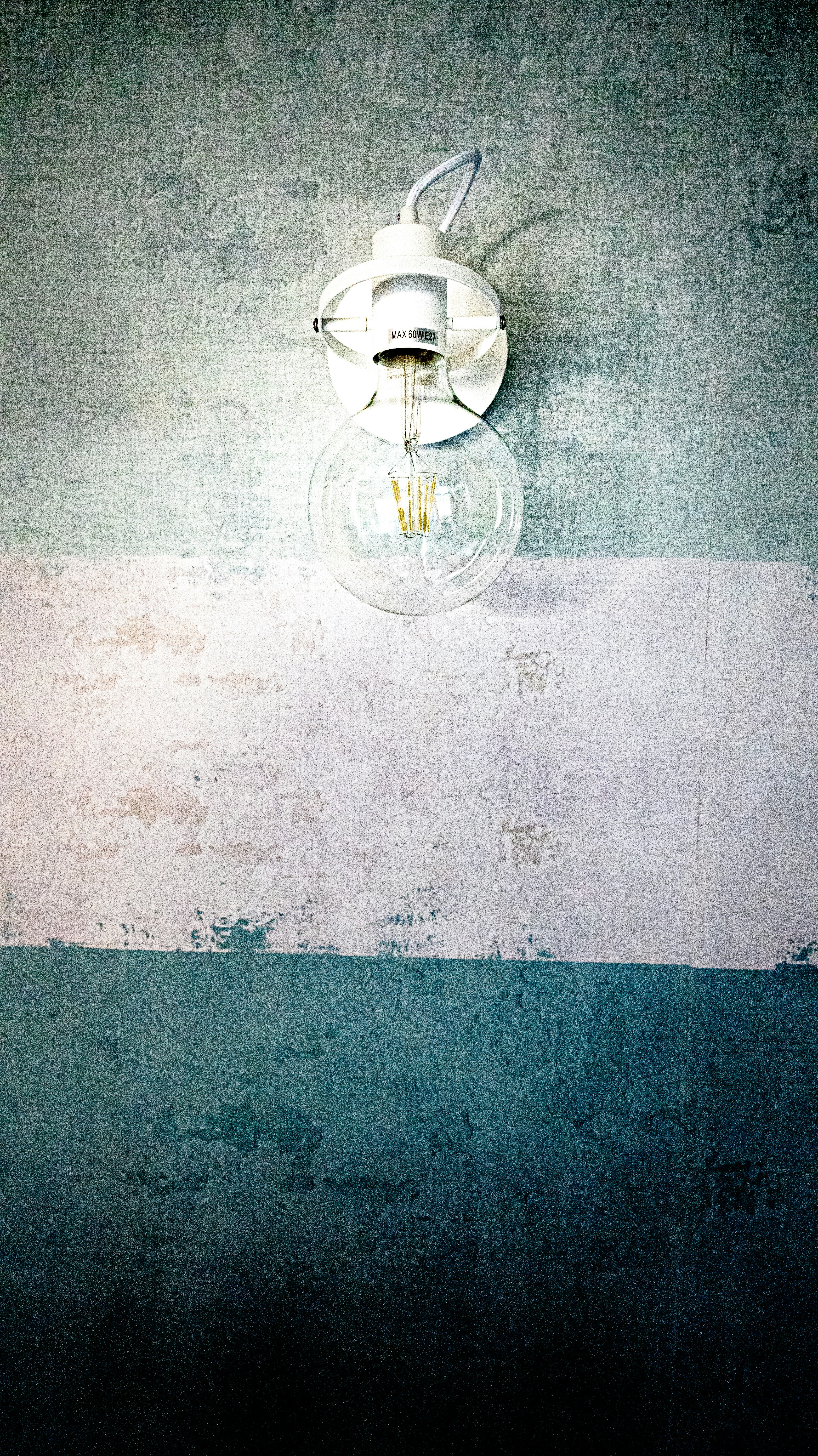 A white wall lamp with exposed bulb on textured wall.