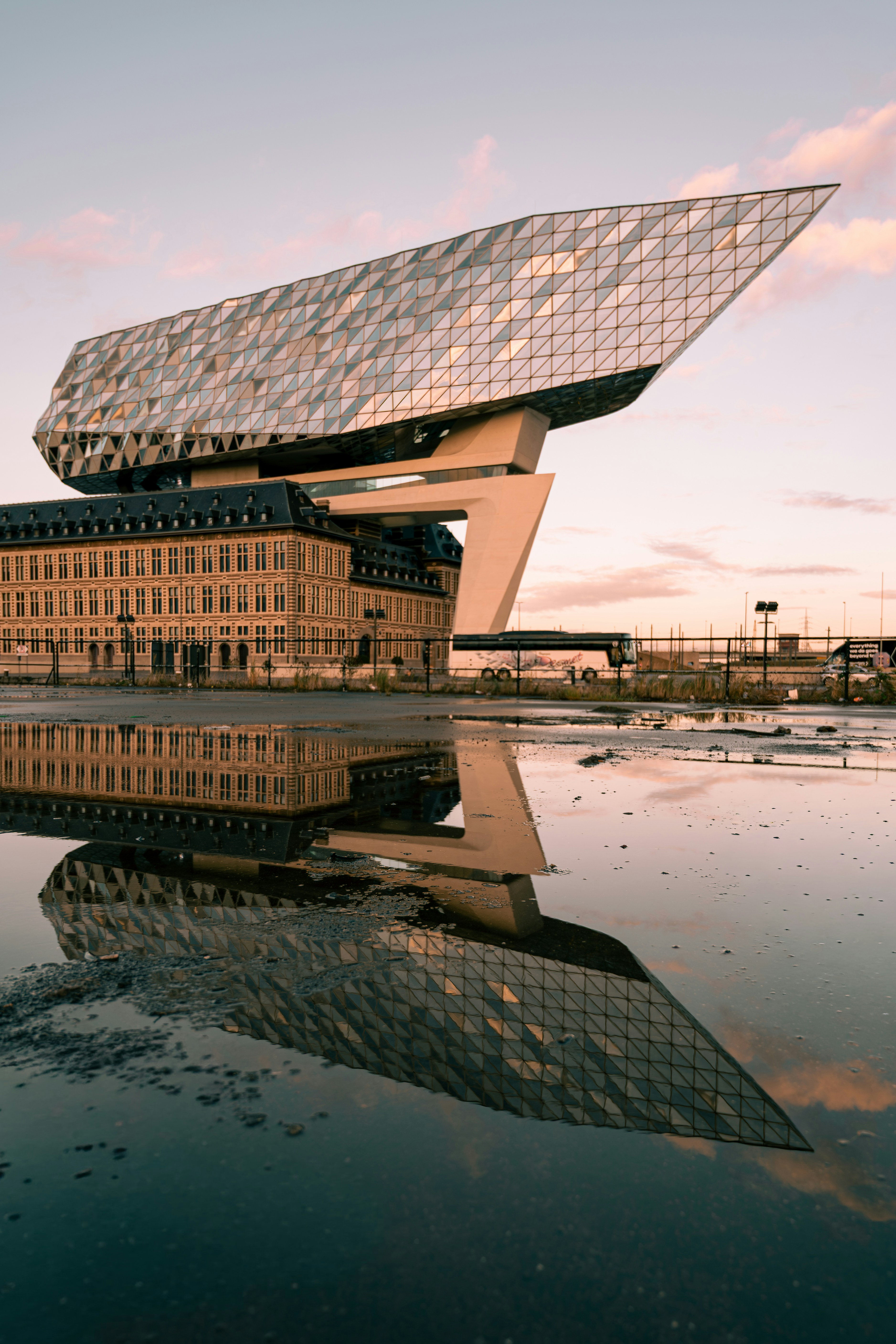 Modern building reflecting in water puddle at sunset
