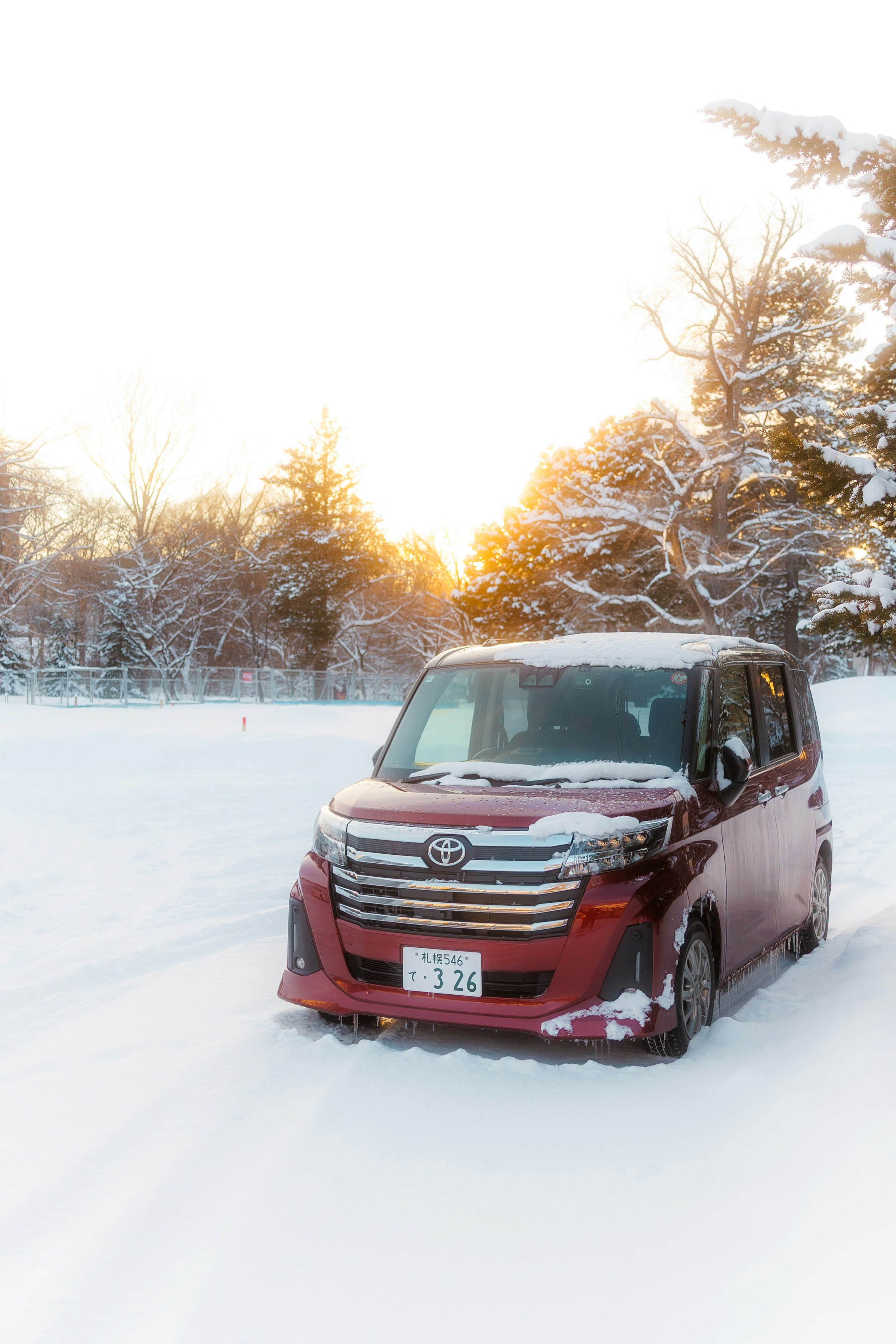 Red car parked in a snowy landscape at sunset.