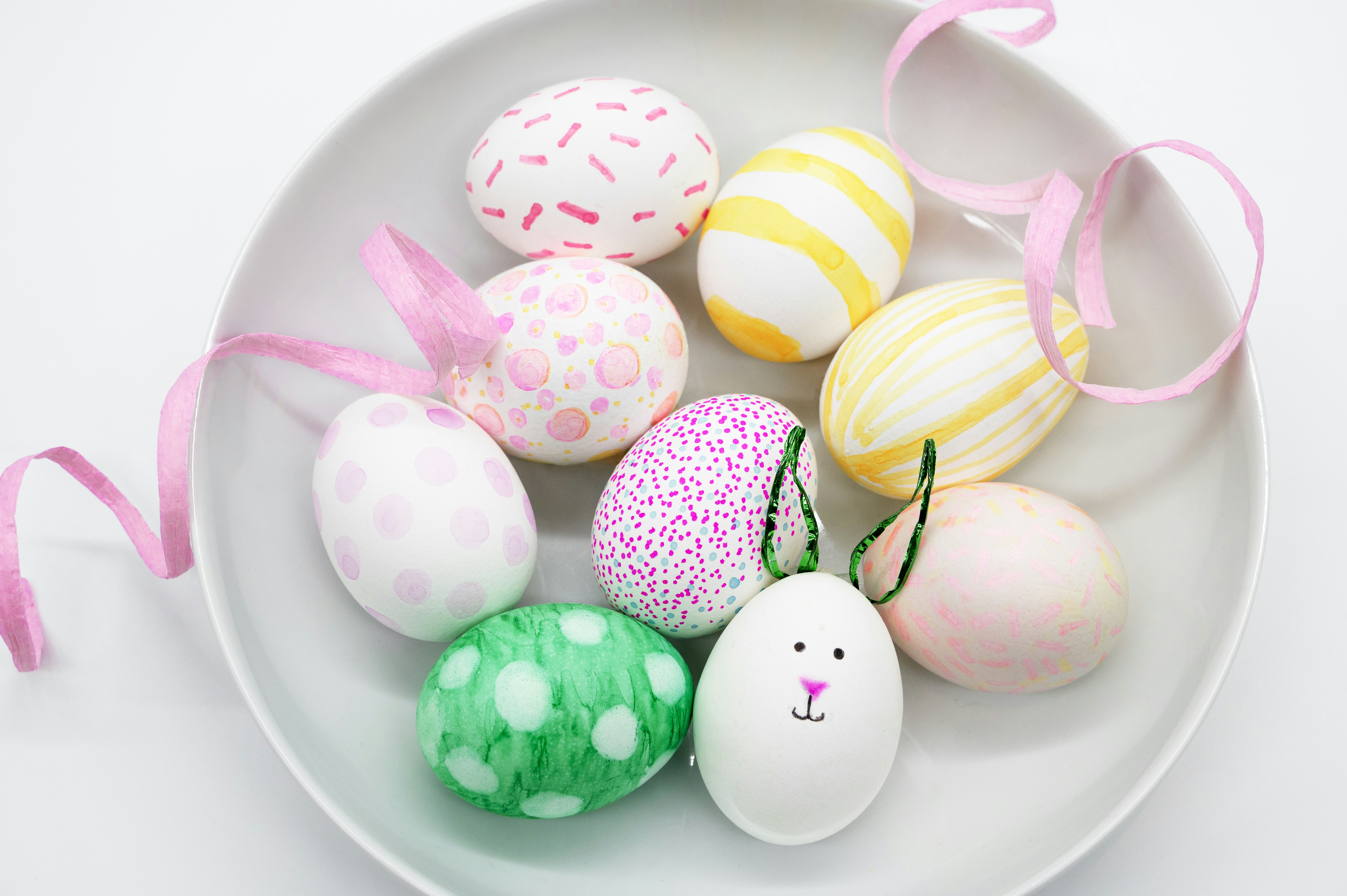 A bowl of decorated easter eggs with ribbons.