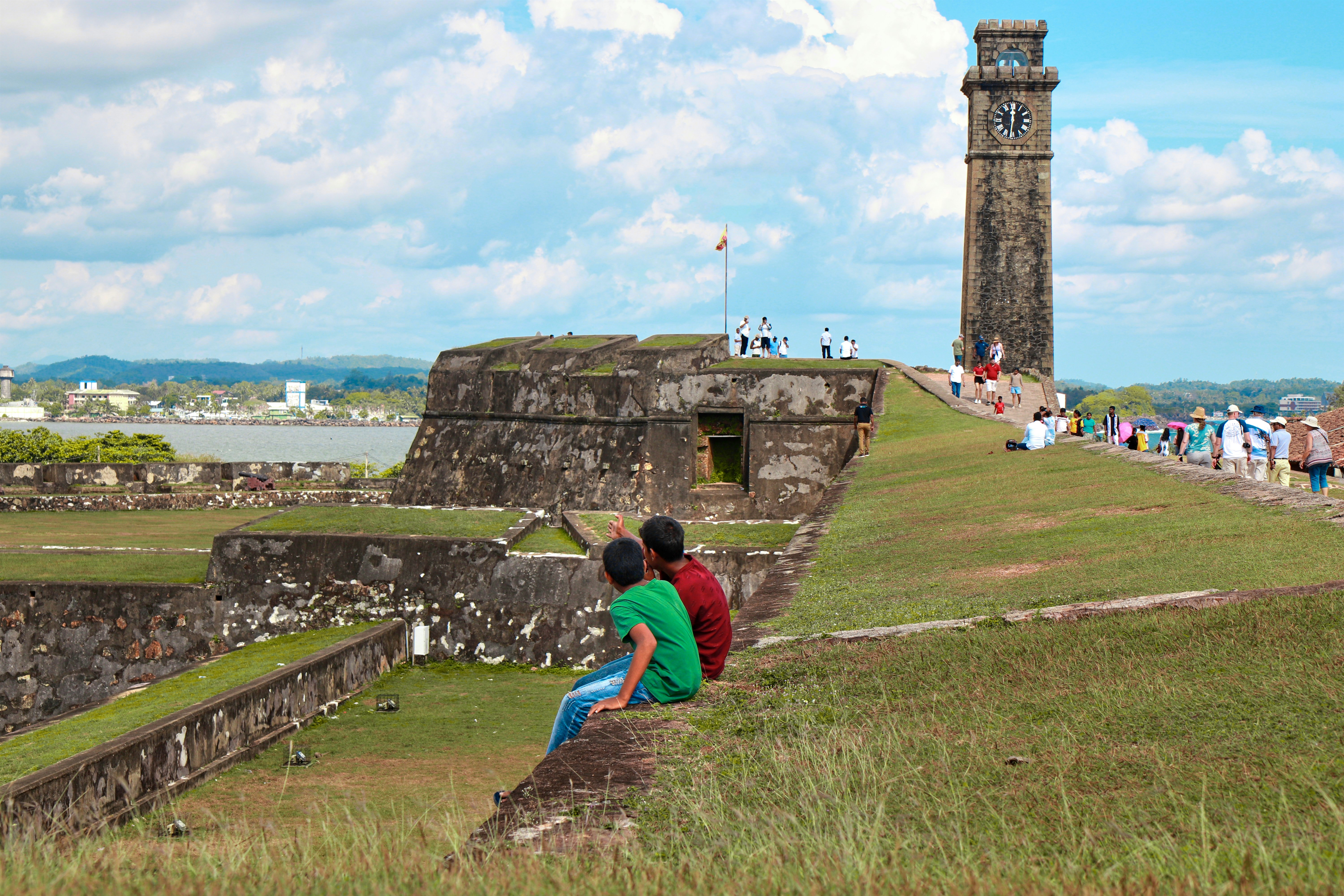 Two people sit on a grassy hill overlooking a fort.