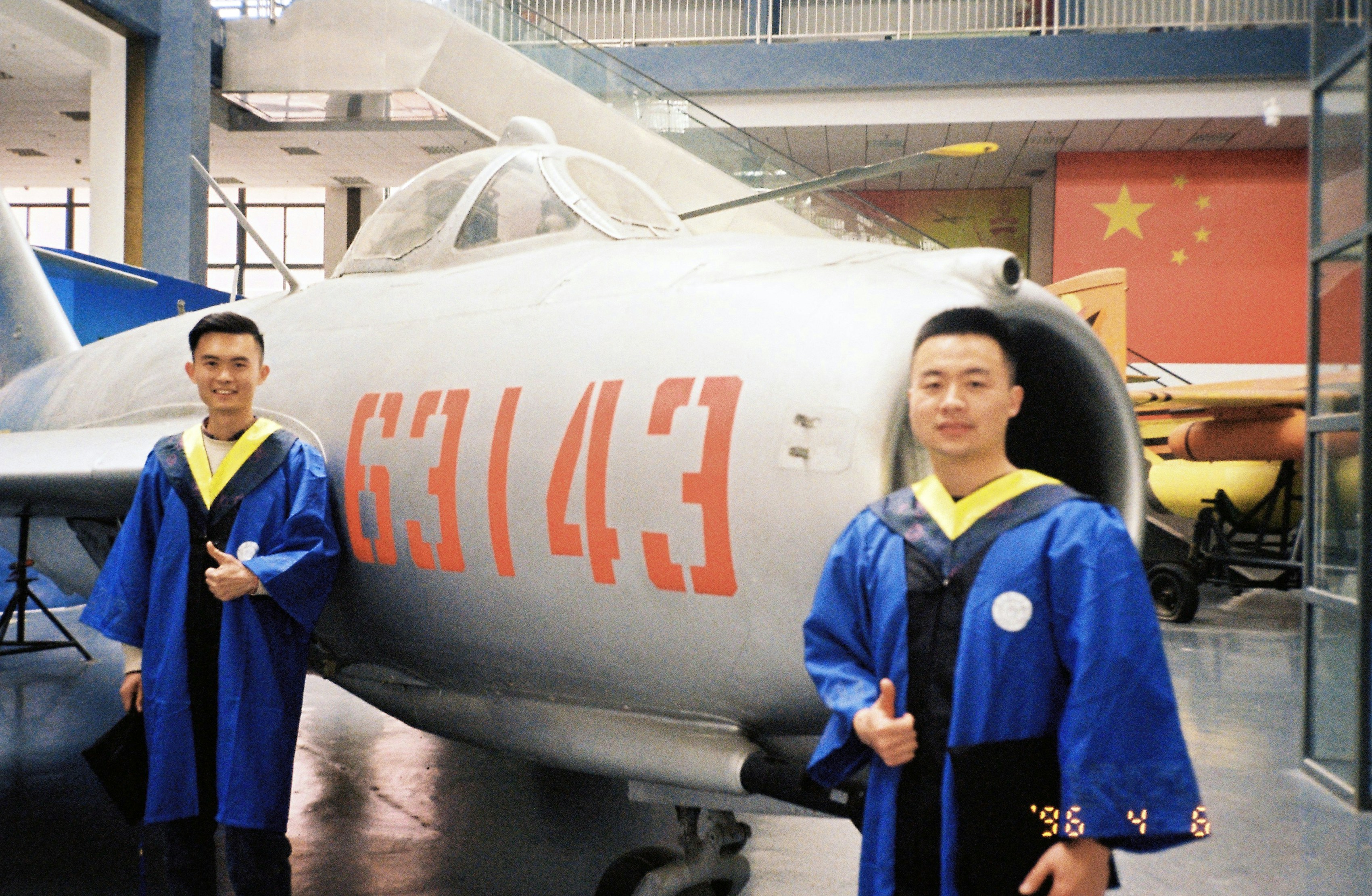 Dos graduados con toga azul están junto a un jet.