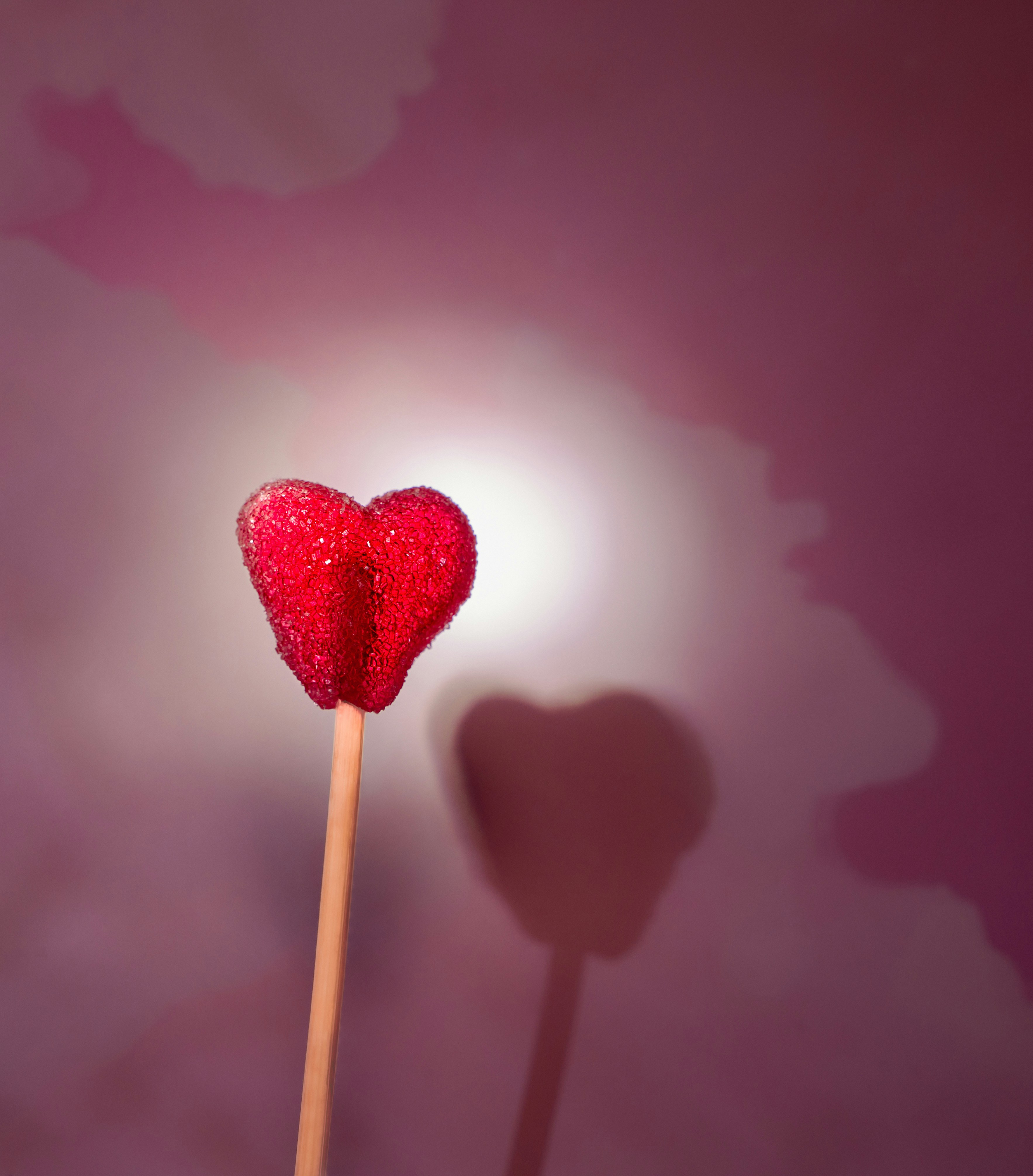 Un lecca-lecca rosso scintillante a forma di cuore proietta un'ombra.