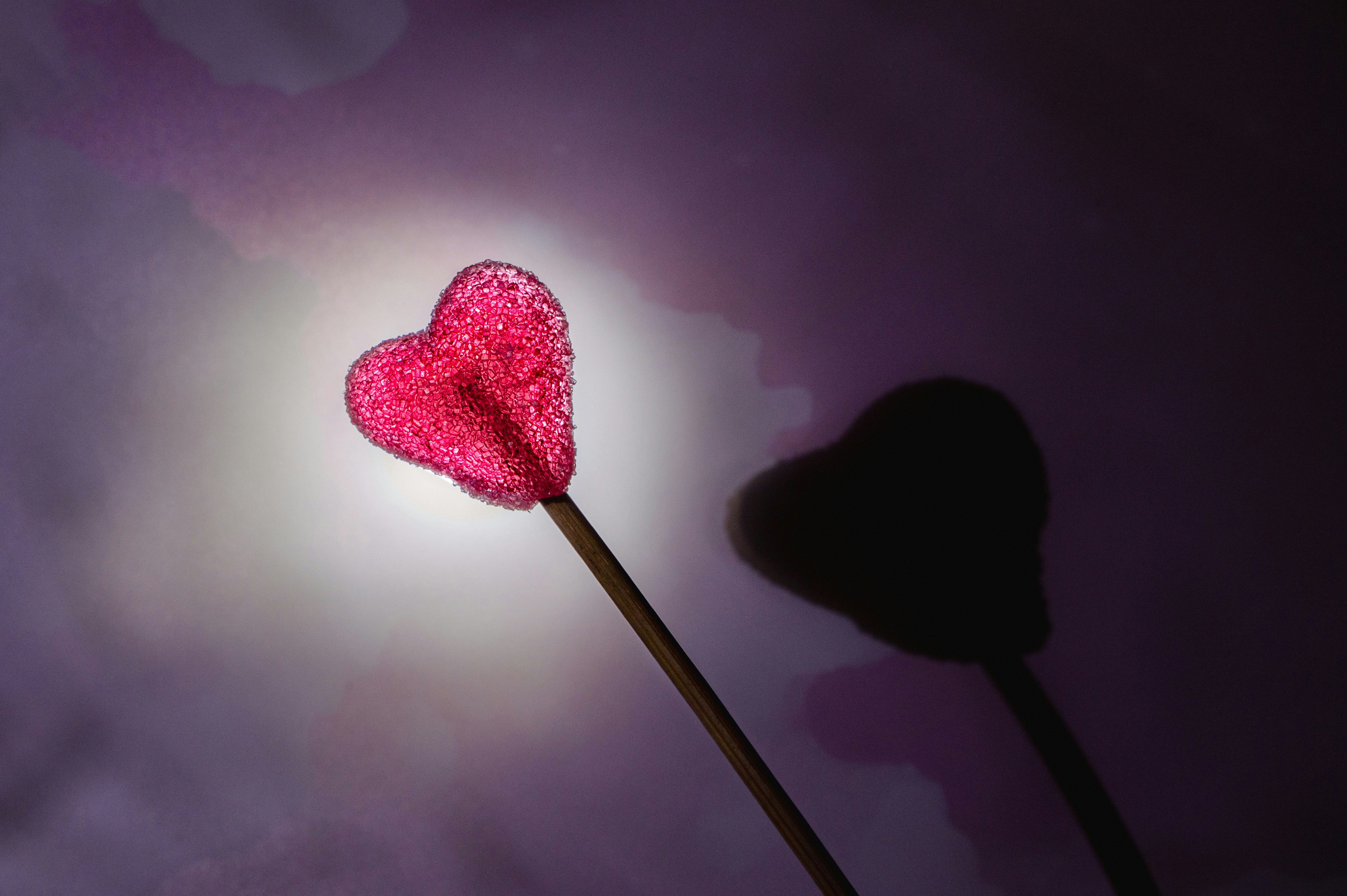 Un lecca-lecca rosa luminoso a forma di cuore con un'ombra.