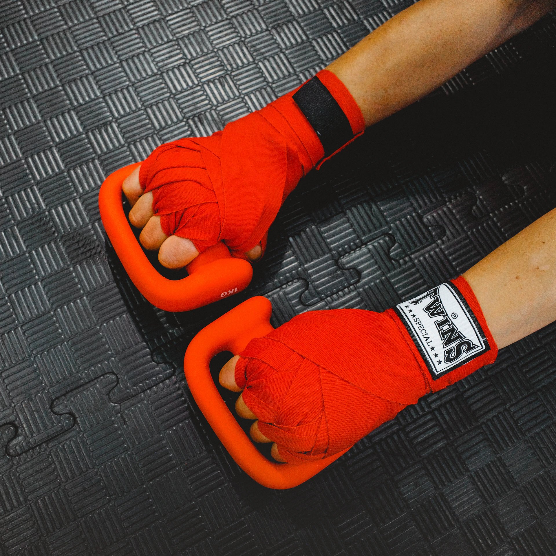 Hands wrapped in red boxing tape holding orange grips