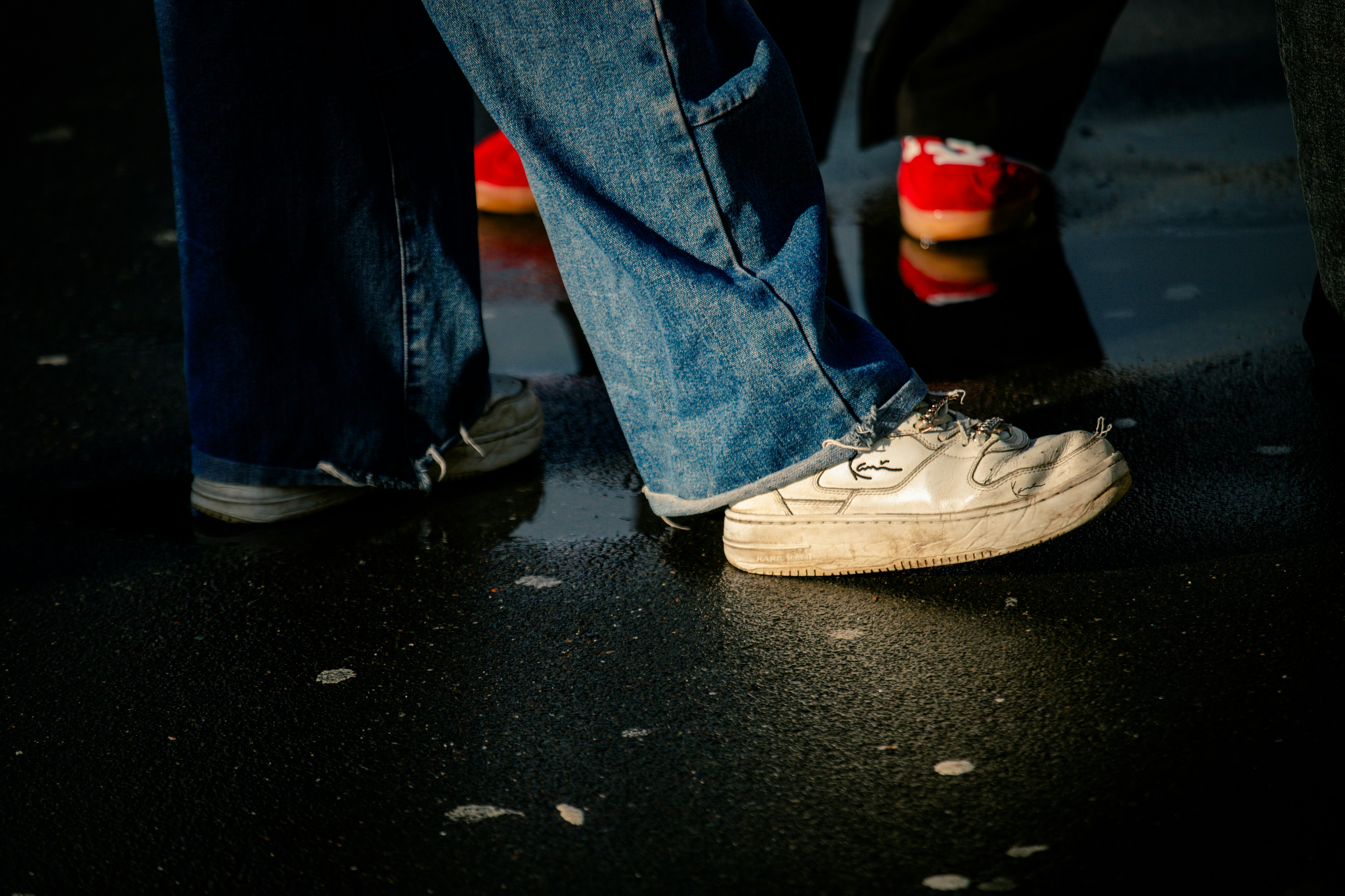 People's feet in jeans and sneakers on wet pavement