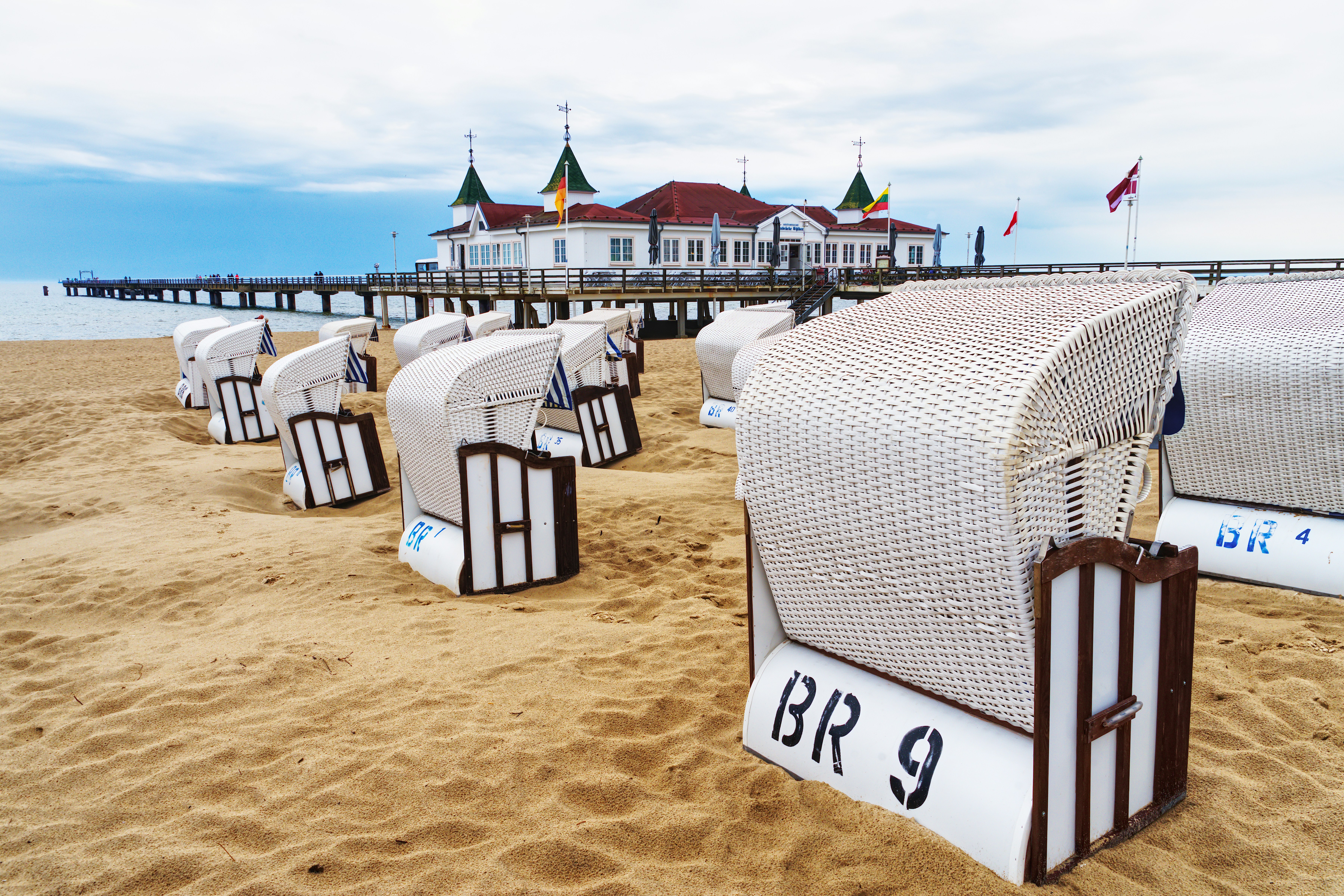 Tumbonas de playa en la orilla arenosa con muelle y edificio.