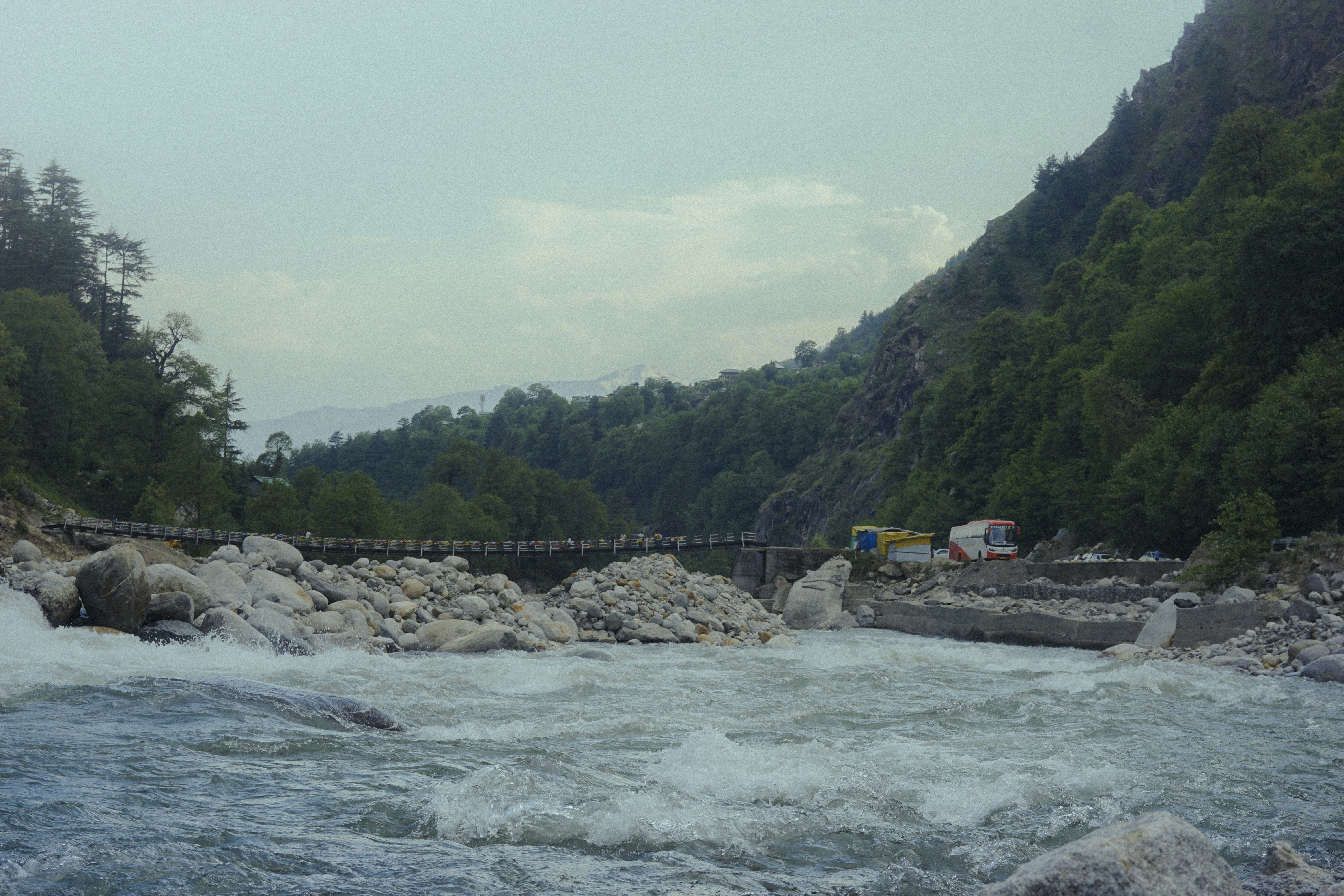 Rushing river flows past rocky shore with distant bridge.